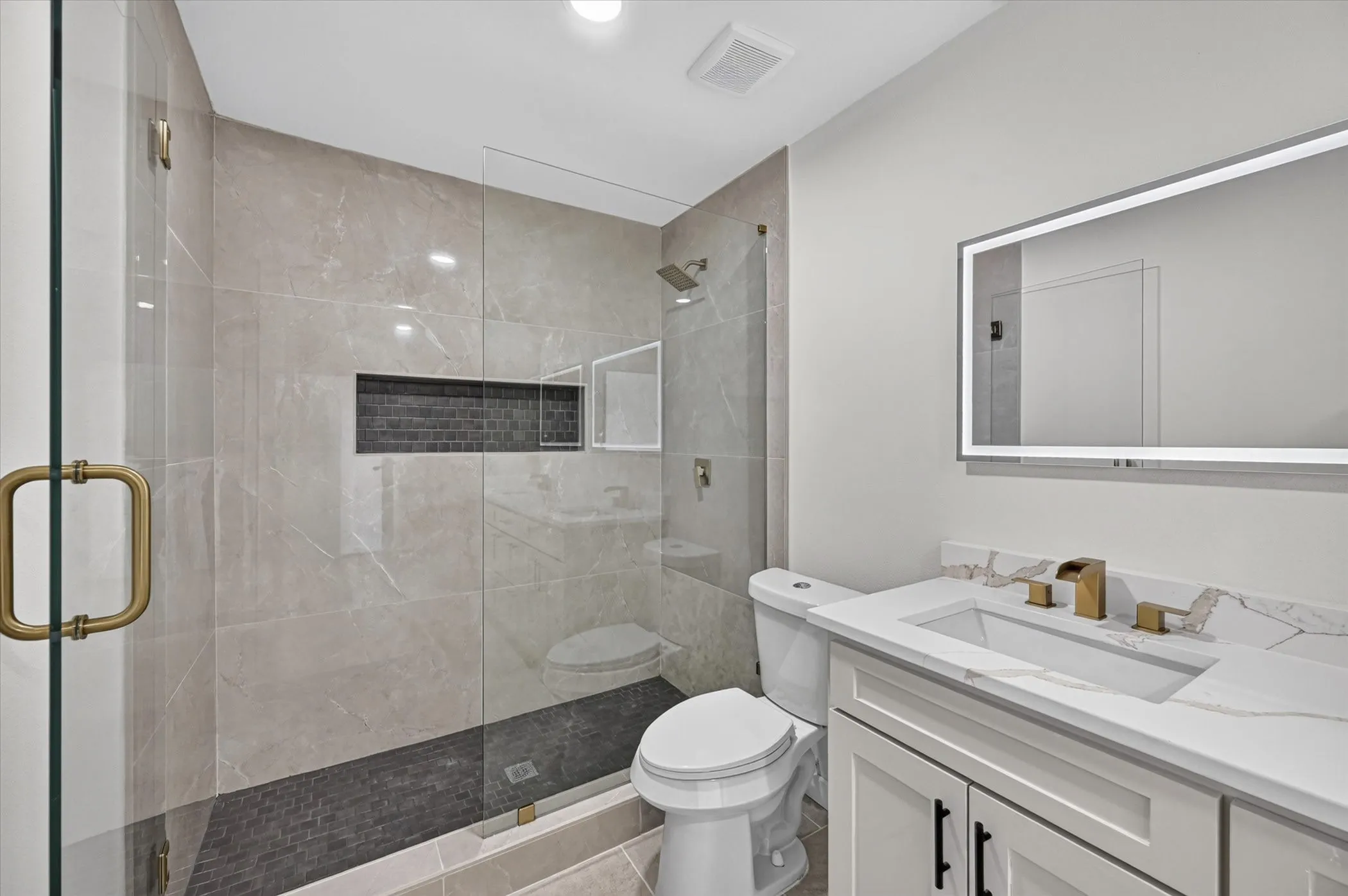 Glass-enclosed shower with a recessed shelf, gold-tone shower fixtures, and a dark mosaic tile floor