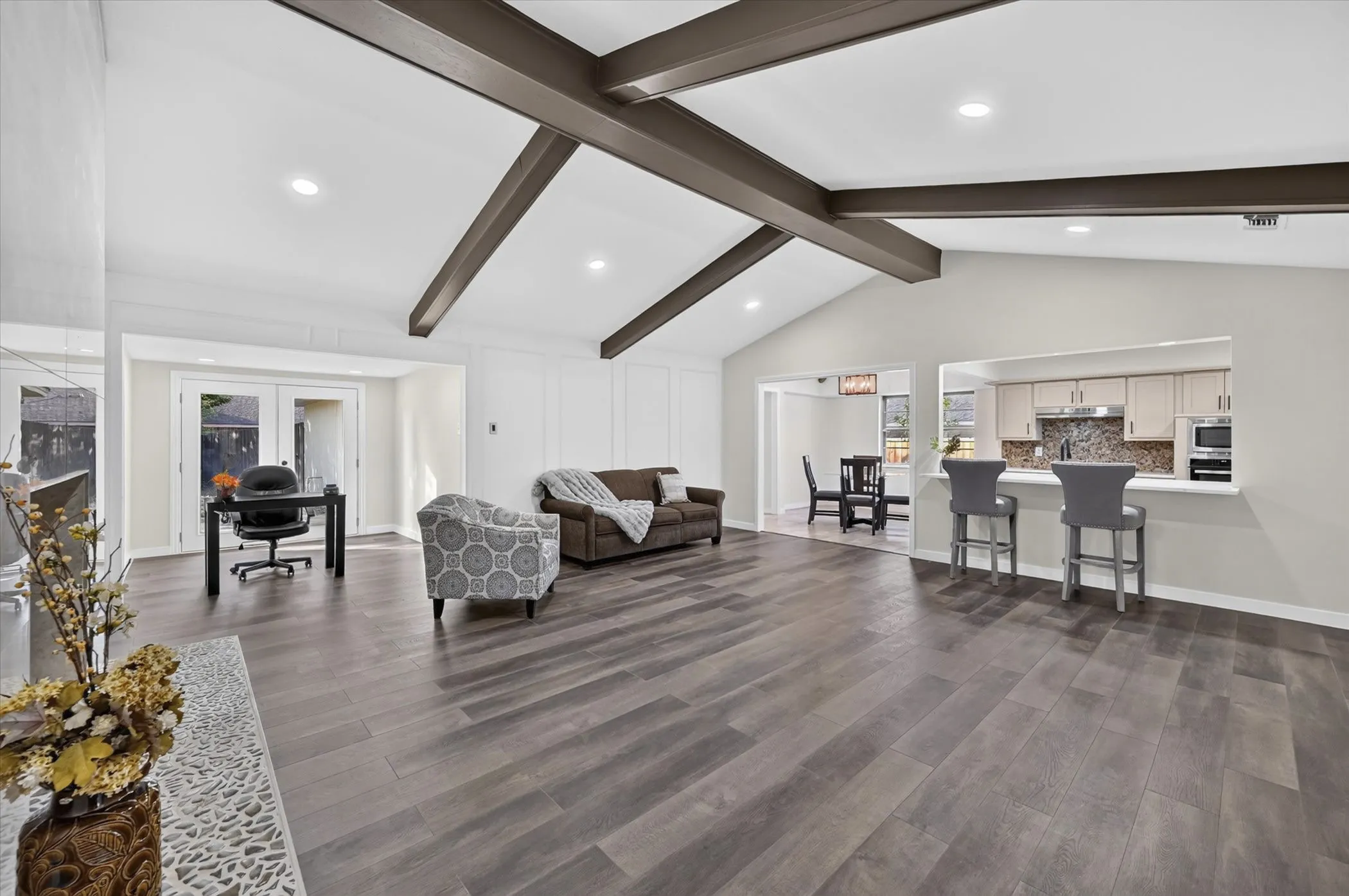 Vaulted ceiling with exposed beams, wood-finish flooring, recessed lighting, and a kitchen pass-through with counter seating