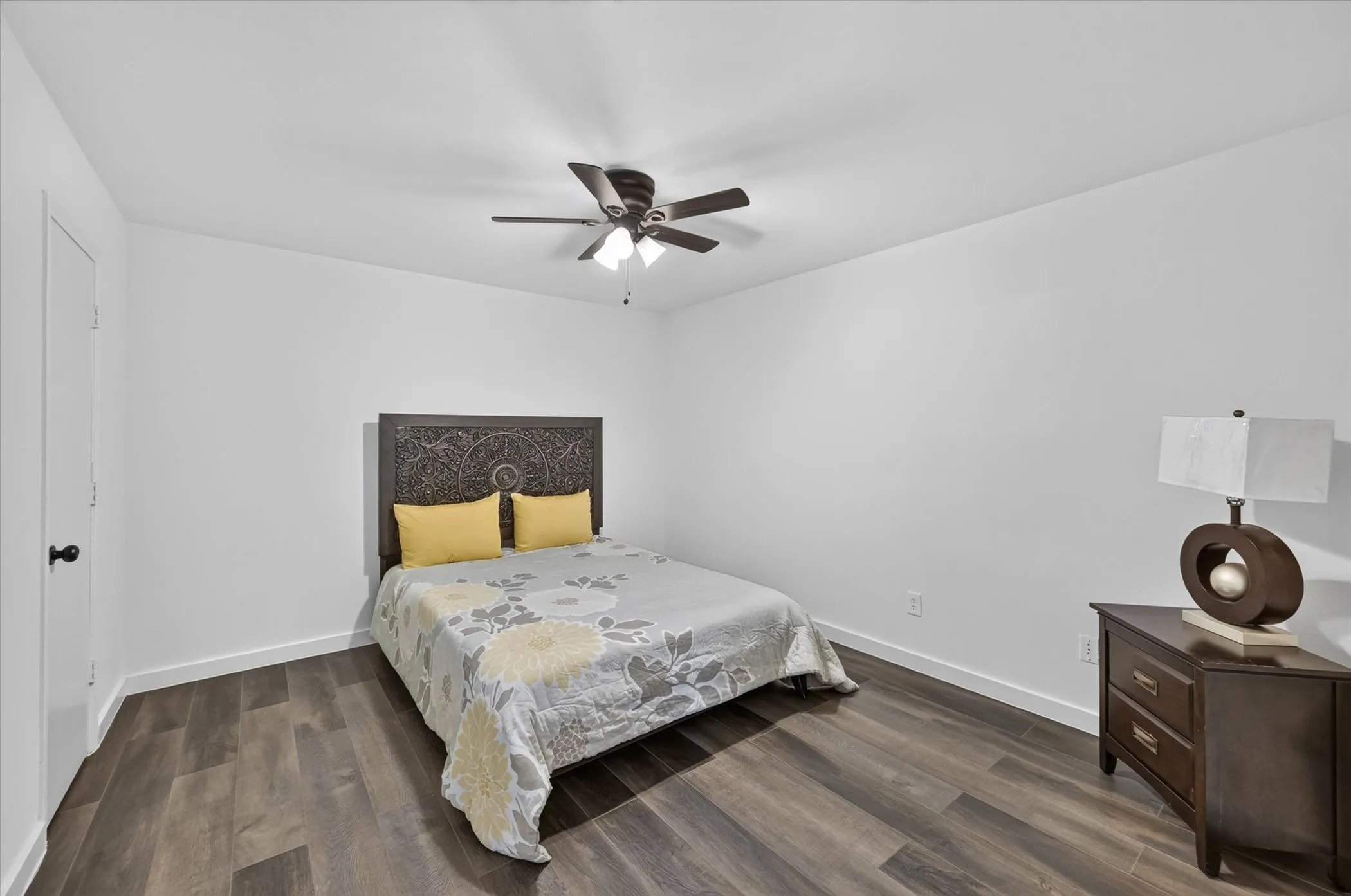 Wood-finish flooring throughout, white painted walls, and a ceiling fan with integrated lighting