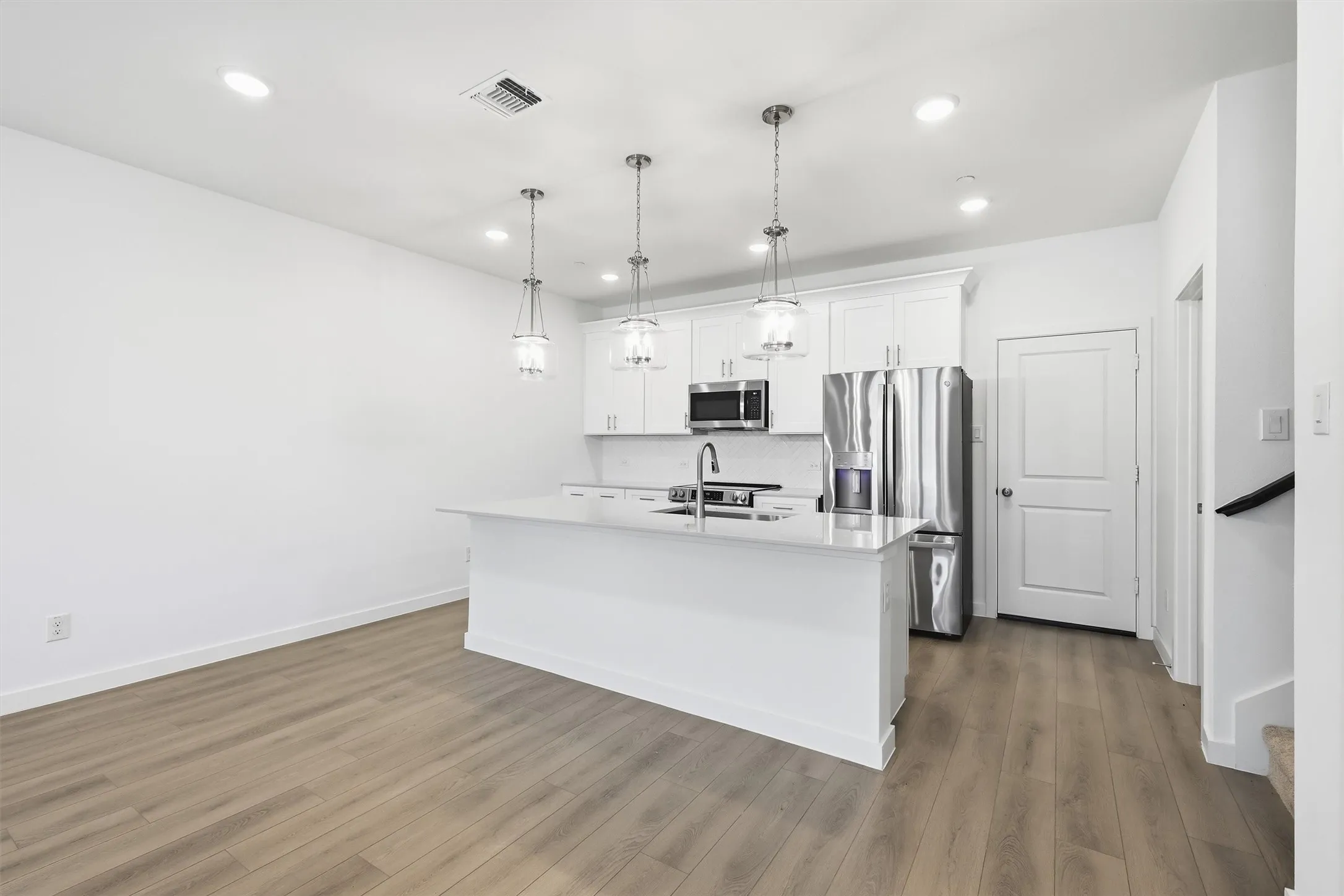 Open-concept kitchen featuring an island with a sink, white cabinetry, stainless steel appliances, and pendant lighting