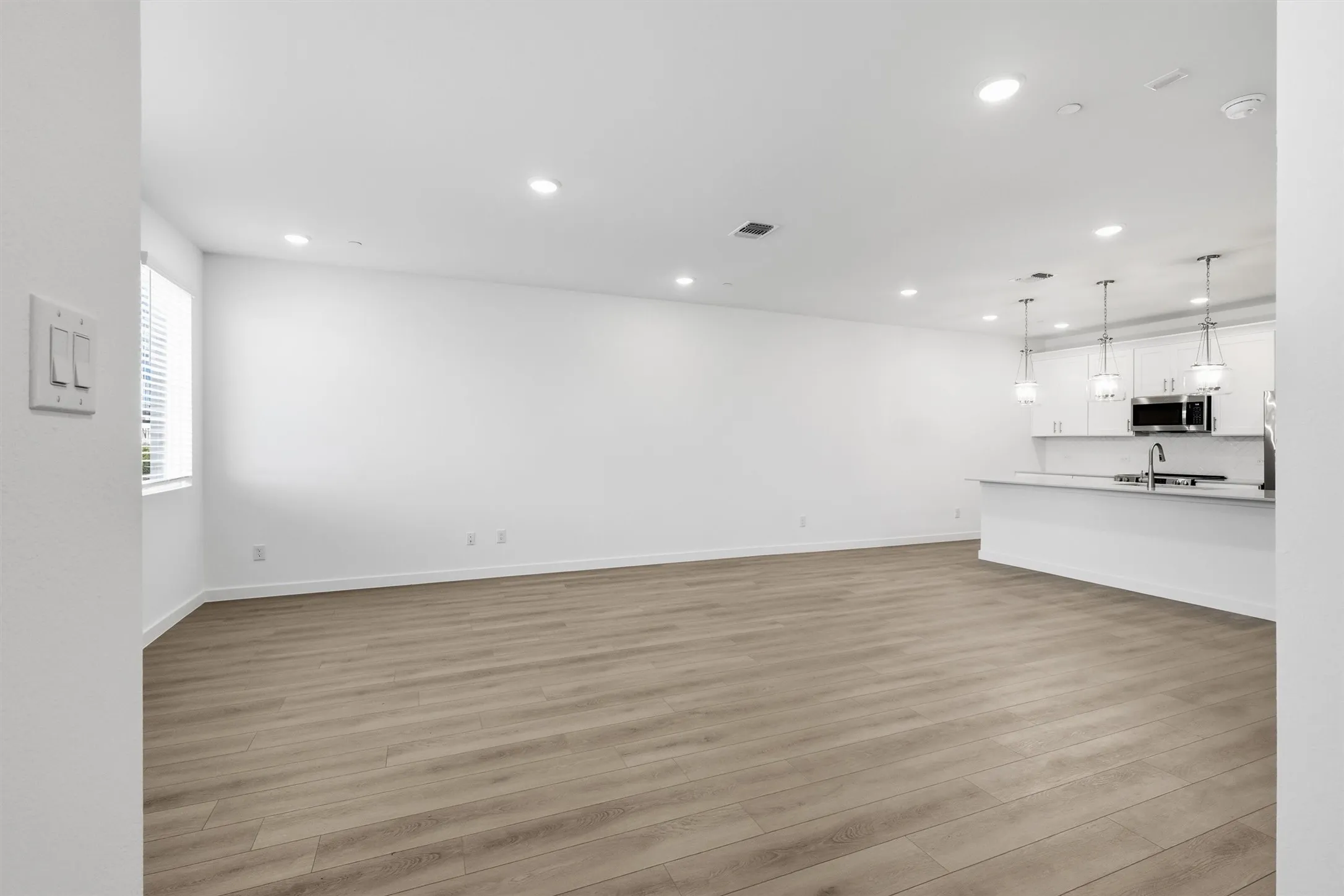 Expansive open-concept space featuring wood-finish flooring, recessed lighting, and a kitchen island with pendant lighting