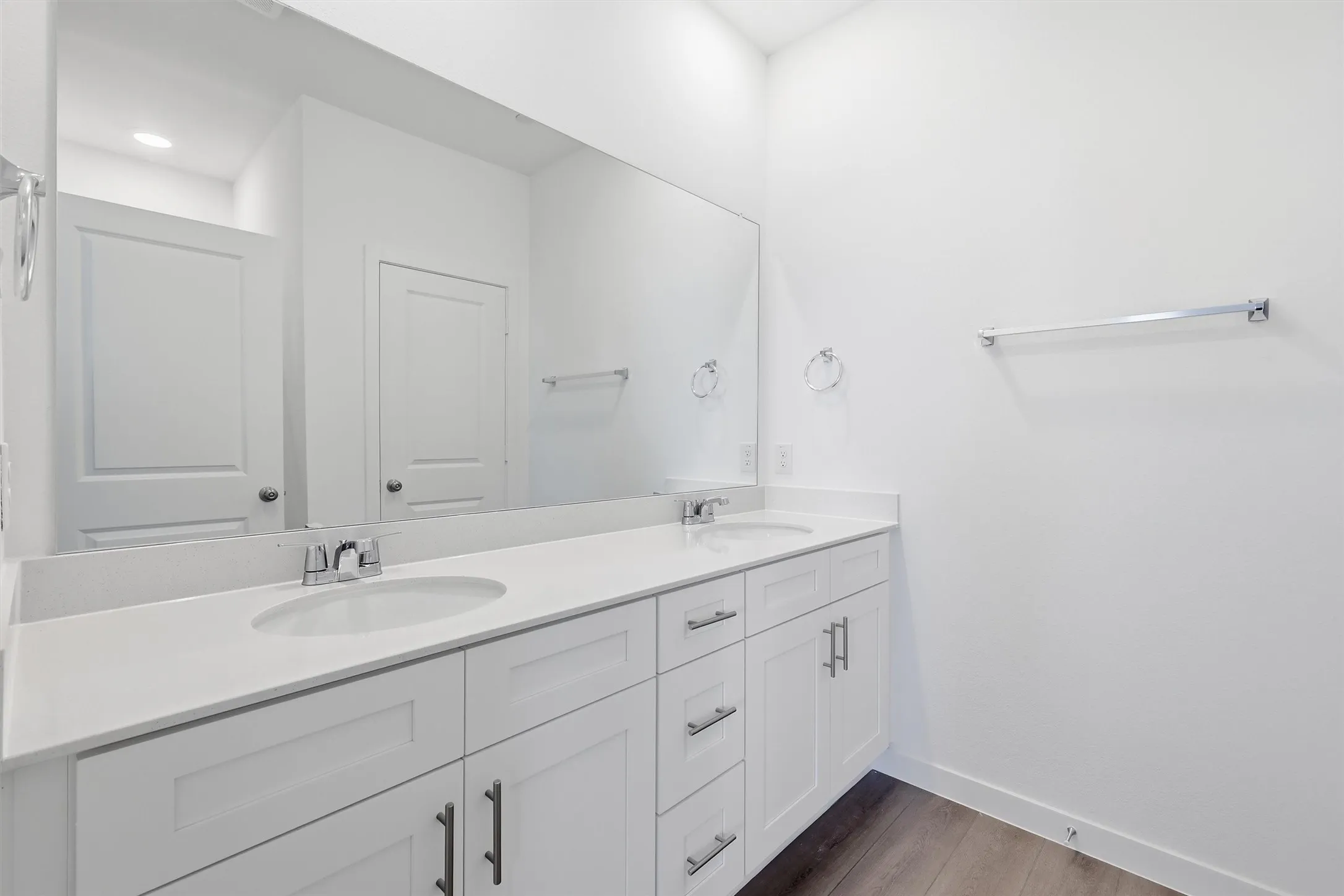 Double vanity with white cabinetry, integrated sinks, chrome fixtures, and a large wall-mounted mirror