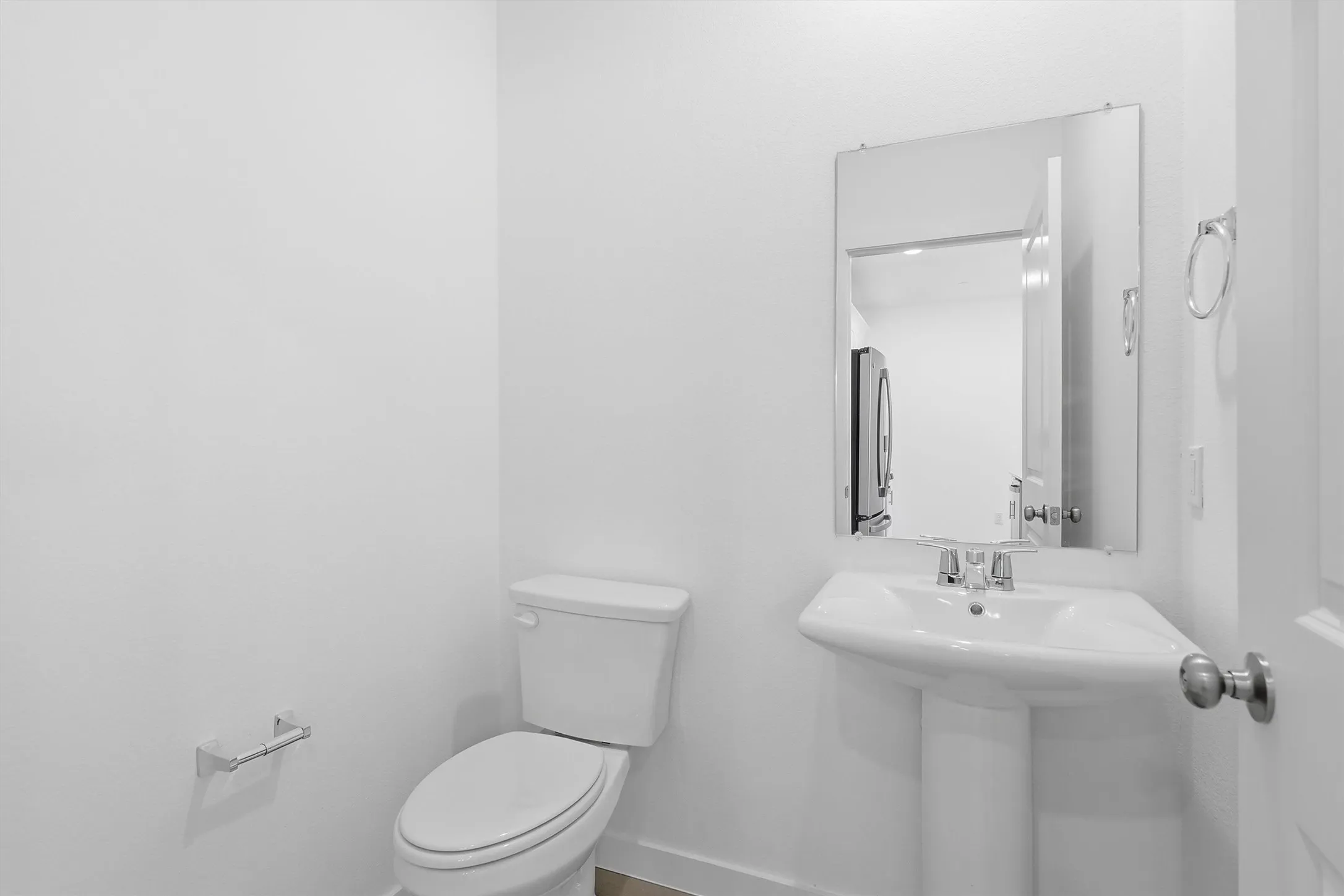 Pedestal sink with chrome faucet, wall-mounted mirror, white toilet, and chrome towel ring