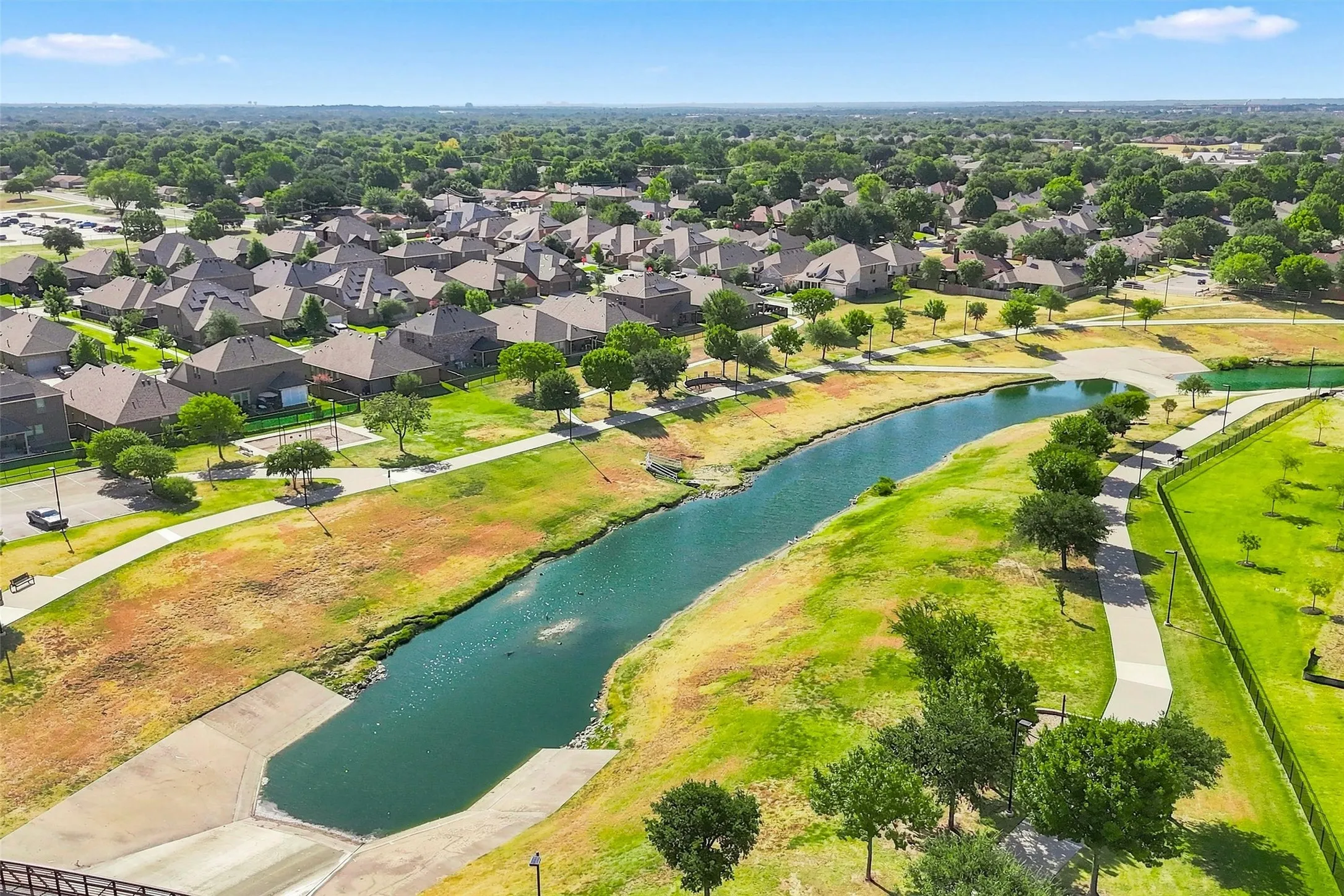 Residential community with mature tree coverage, featuring a water channel, pedestrian pathways, and open green spaces