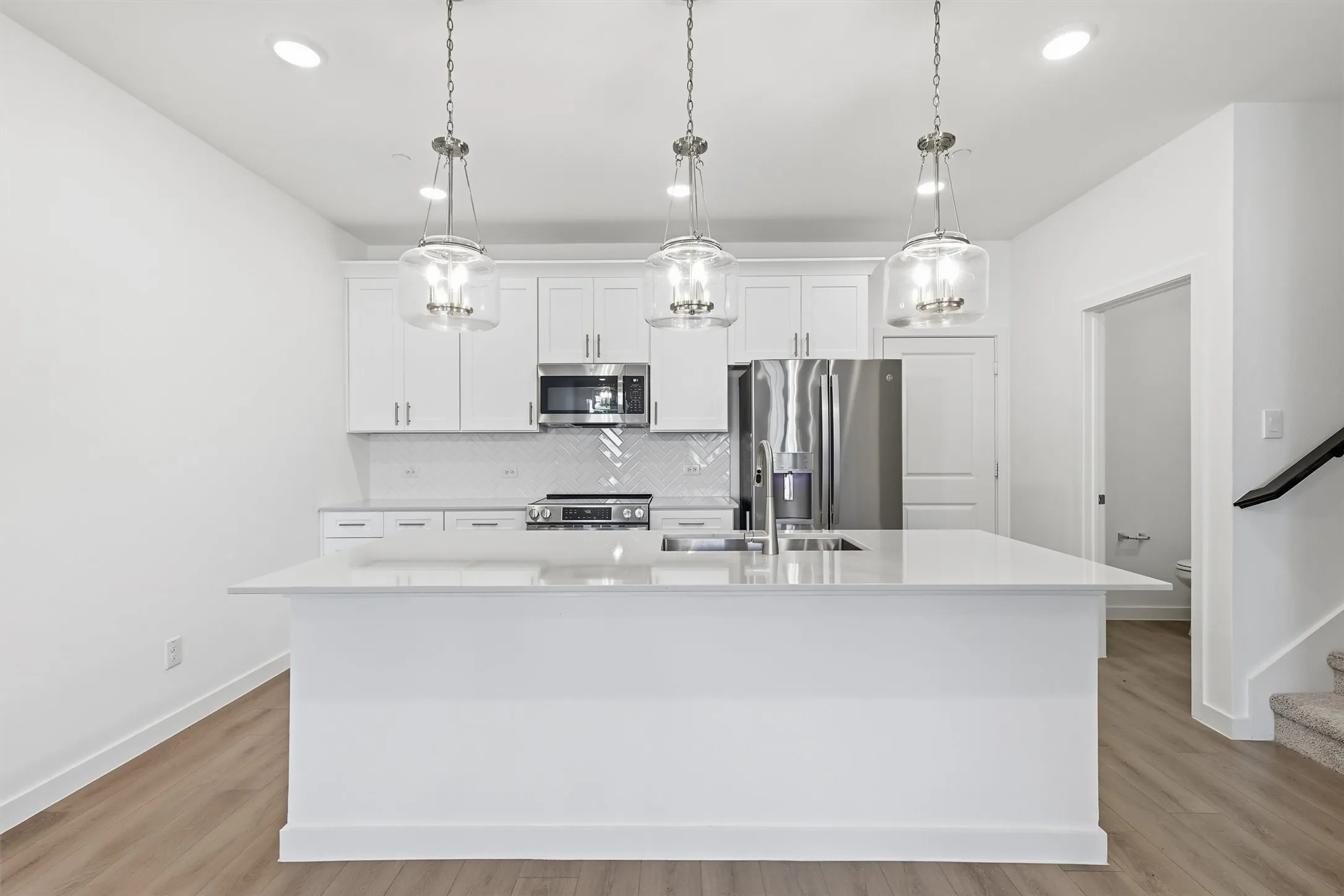 Kitchen featuring an island with a built-in sink, white cabinetry, stainless steel appliances, and wood-finish flooring