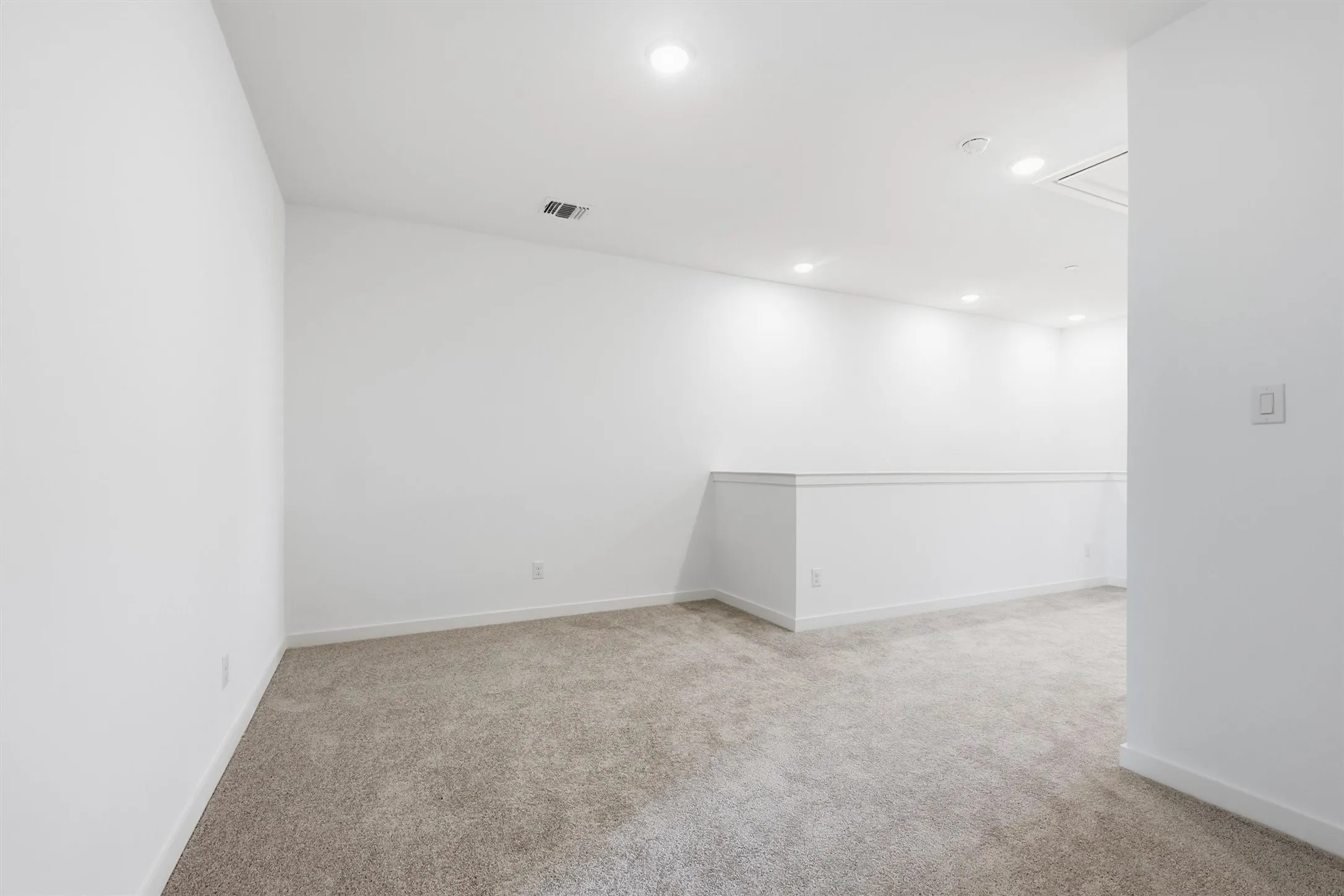 Carpeted room with recessed lighting and a white half-wall