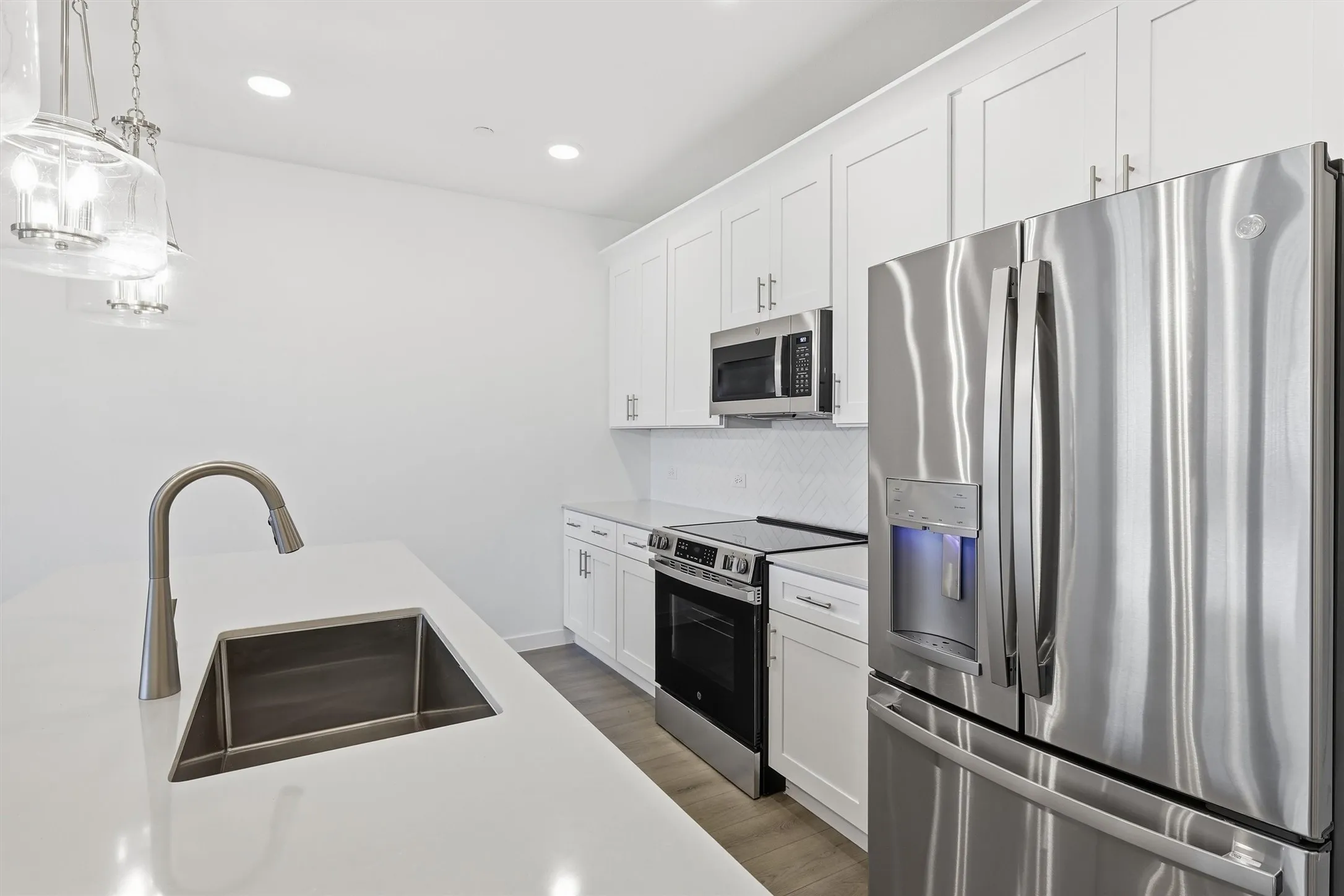 White cabinetry with brushed nickel hardware, stainless steel appliances, white countertops, tile backsplash, and wood-finish flooring