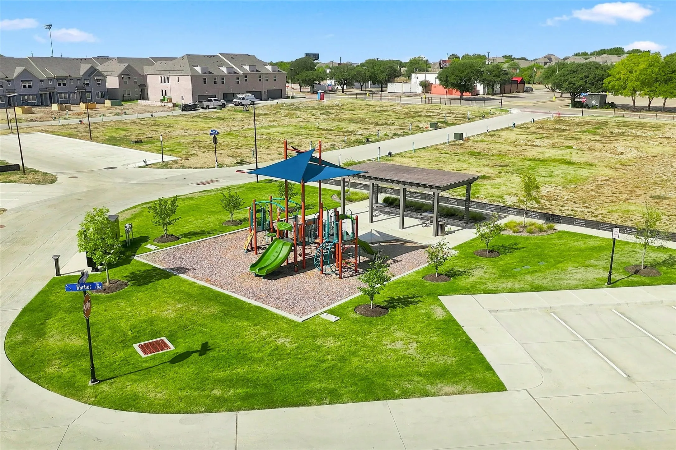 Community playground with a shaded play structure, covered seating area, paved walking paths, and adjacent parking