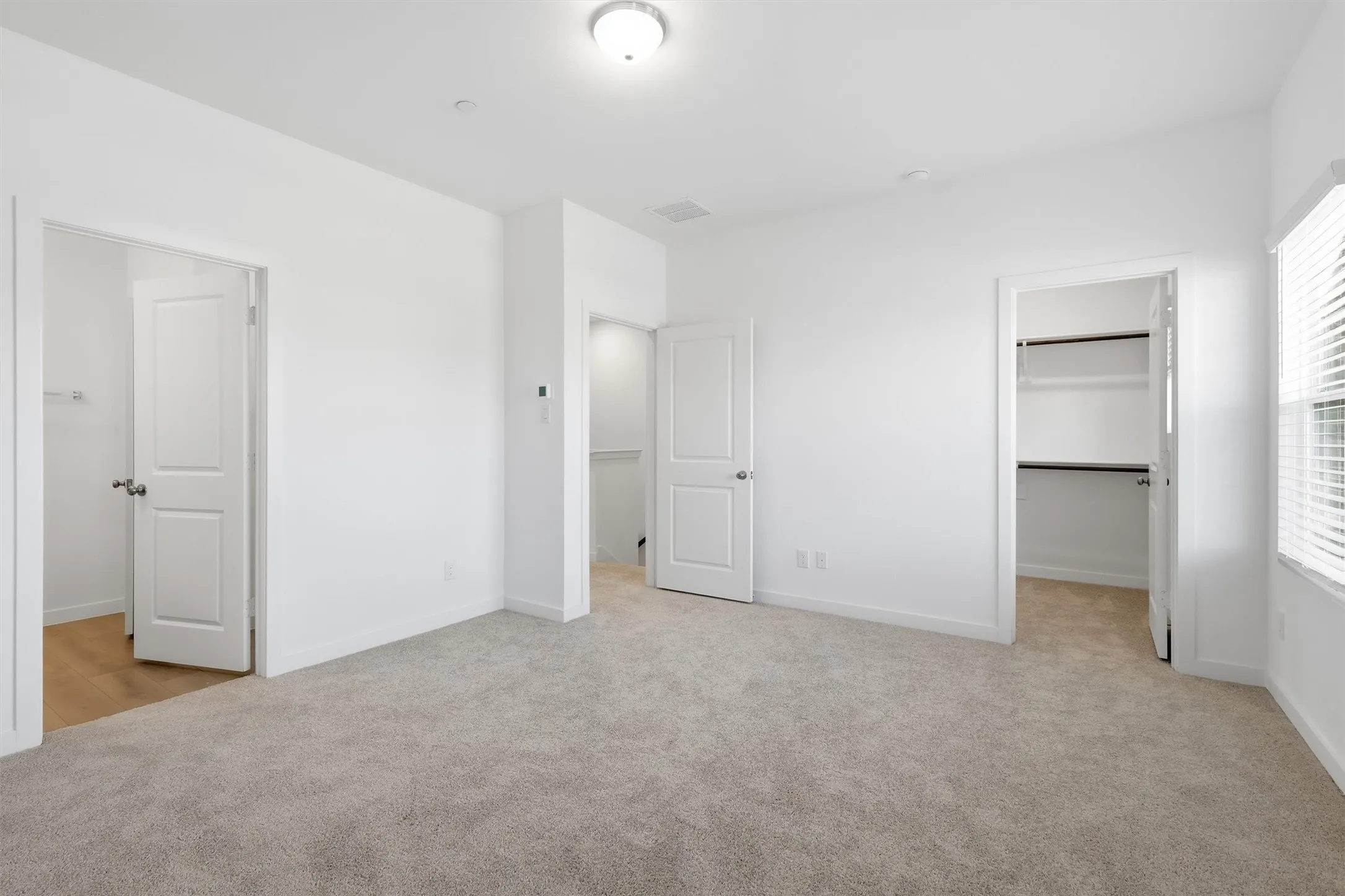 Wall-to-wall carpeting, window with blinds, overhead lighting, and two separate closet spaces featuring built-in shelving