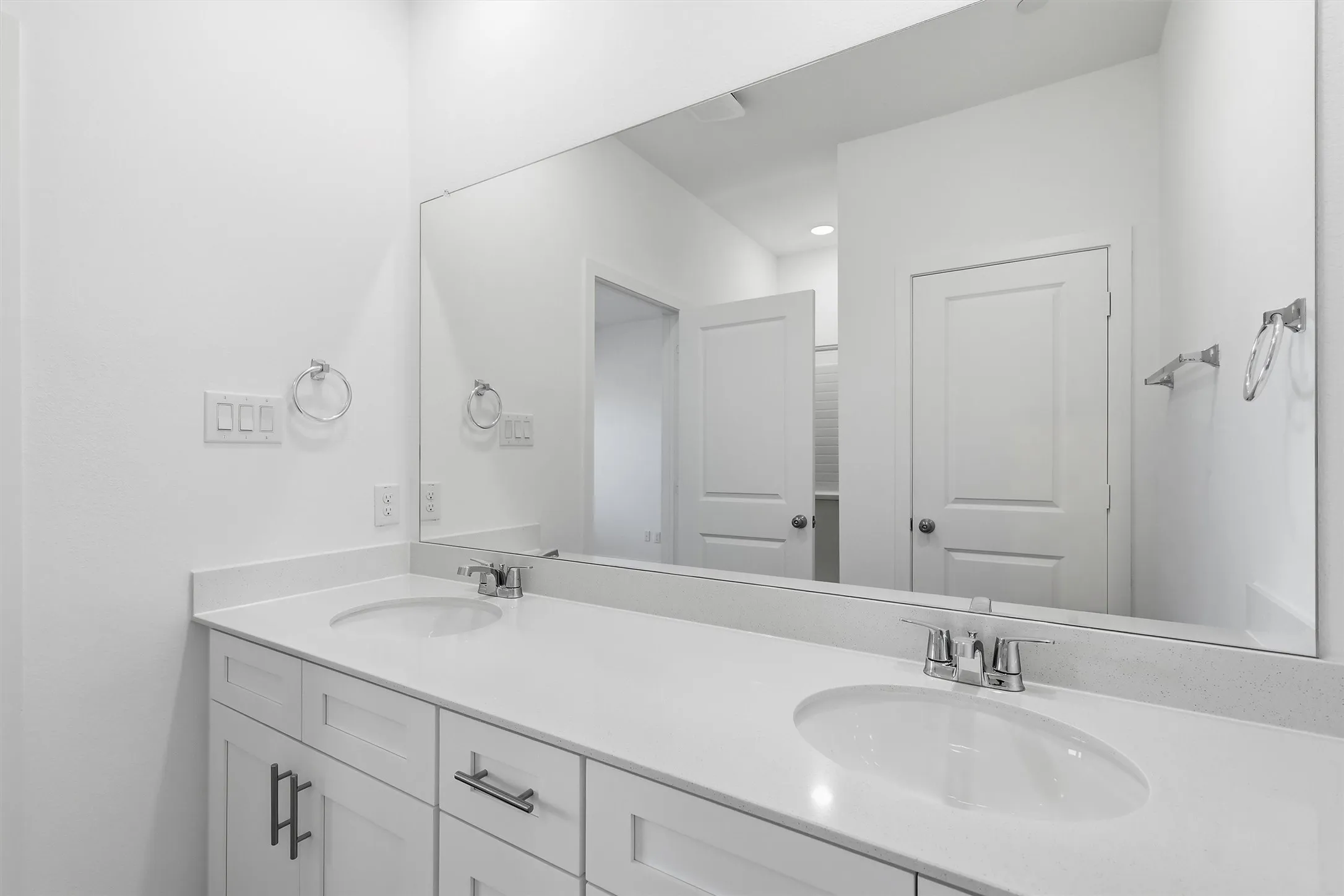 Dual undermount sinks with chrome fixtures, white cabinetry, a light-toned countertop, and a full-width mirror