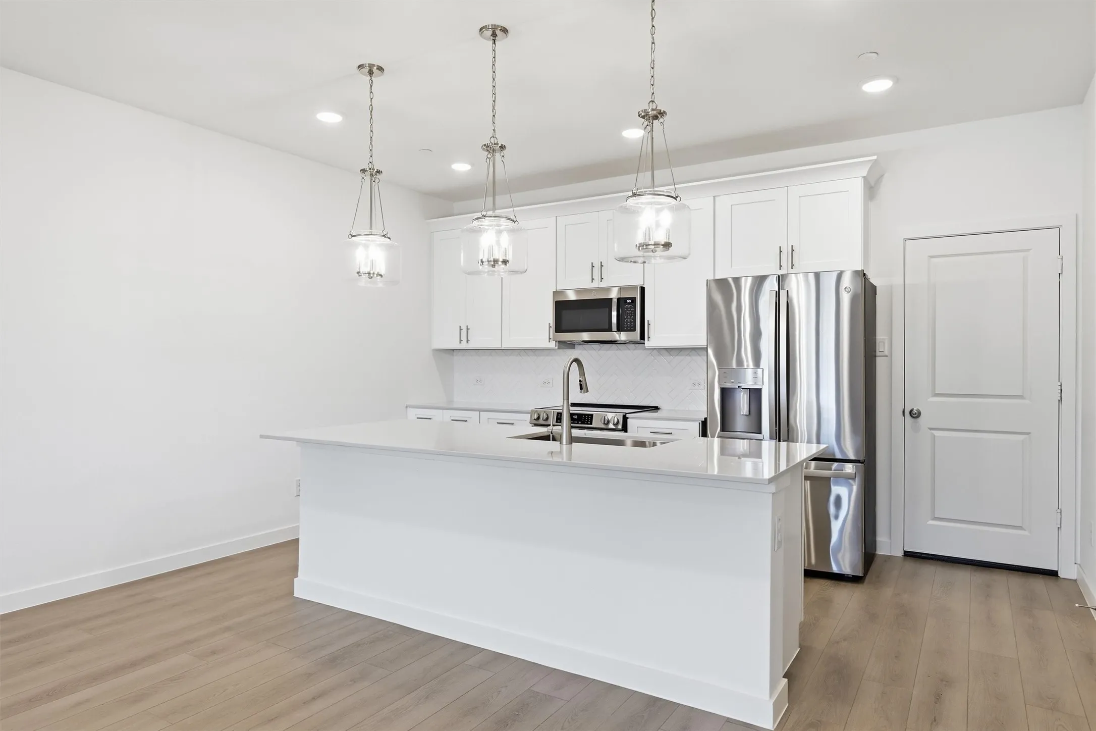Kitchen featuring an island with a built-in sink, white cabinetry, stainless steel appliances, and wood-finish flooring