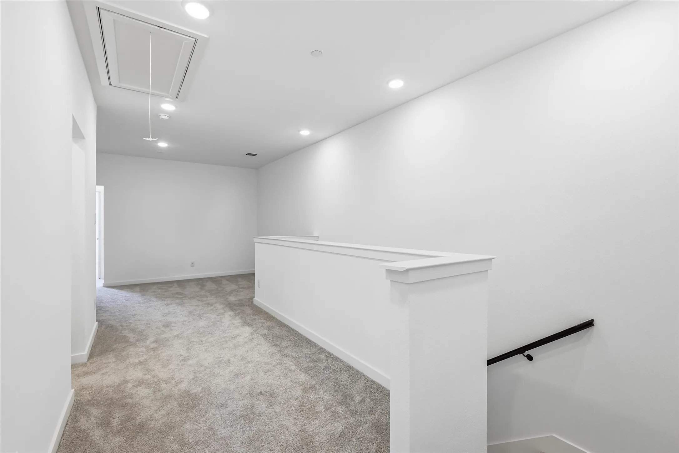 Carpeted hallway with a white half-wall railing, recessed ceiling lighting, and a black handrail