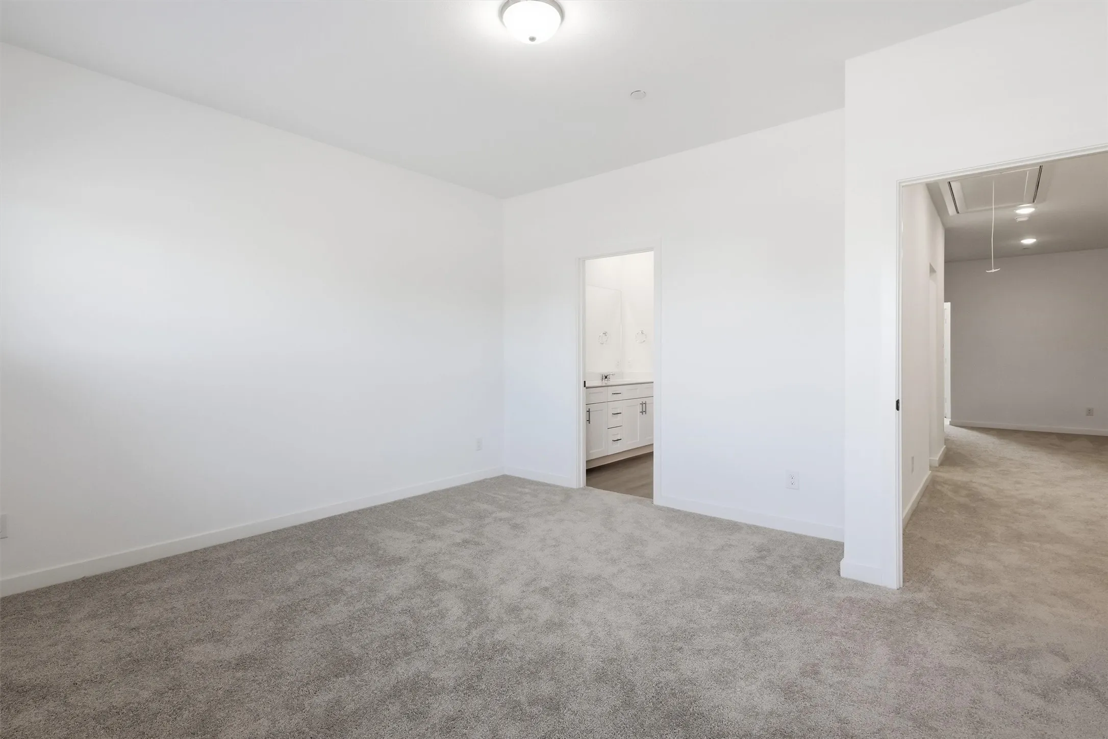 Neutral-toned carpet flooring, white painted walls, ceiling-mounted light fixture, recessed lighting, and a bathroom entrance with a vanity
