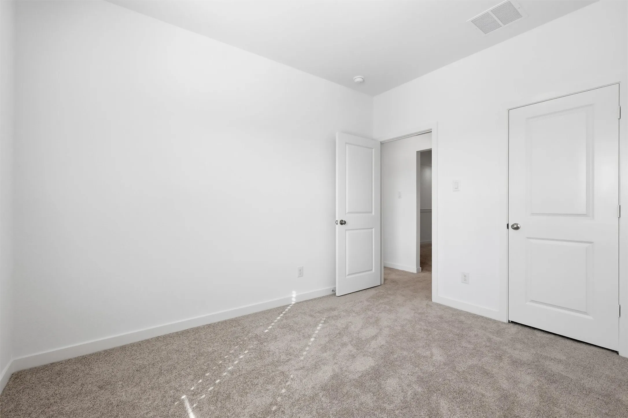 Neutral tone wall paint, light-colored carpet flooring, white trim, and white paneled doors with hardware