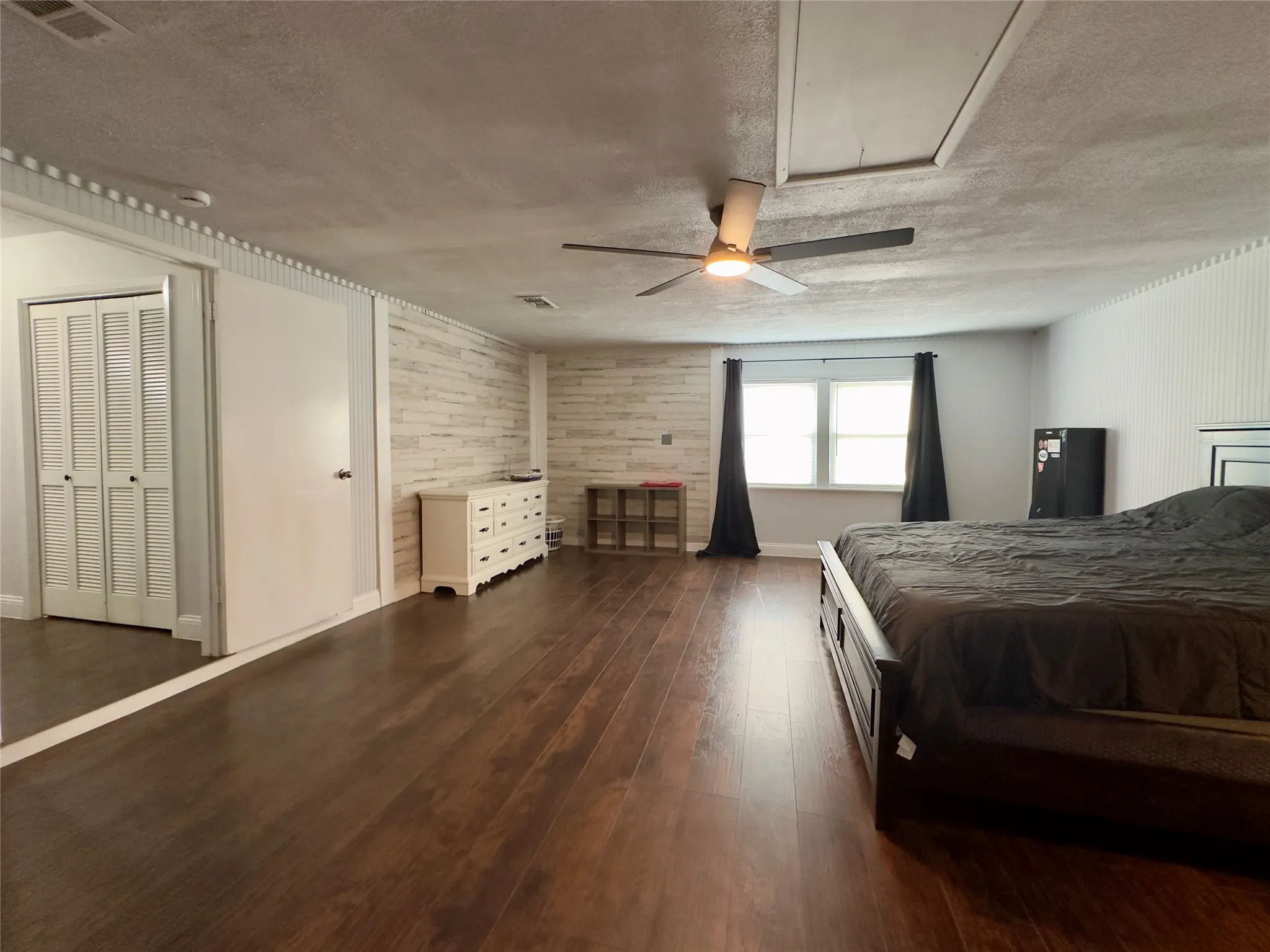 Wood-finish flooring throughout, white horizontal shiplap accent wall, white vertical paneling, dual windows, and ceiling fan with integrated lighting