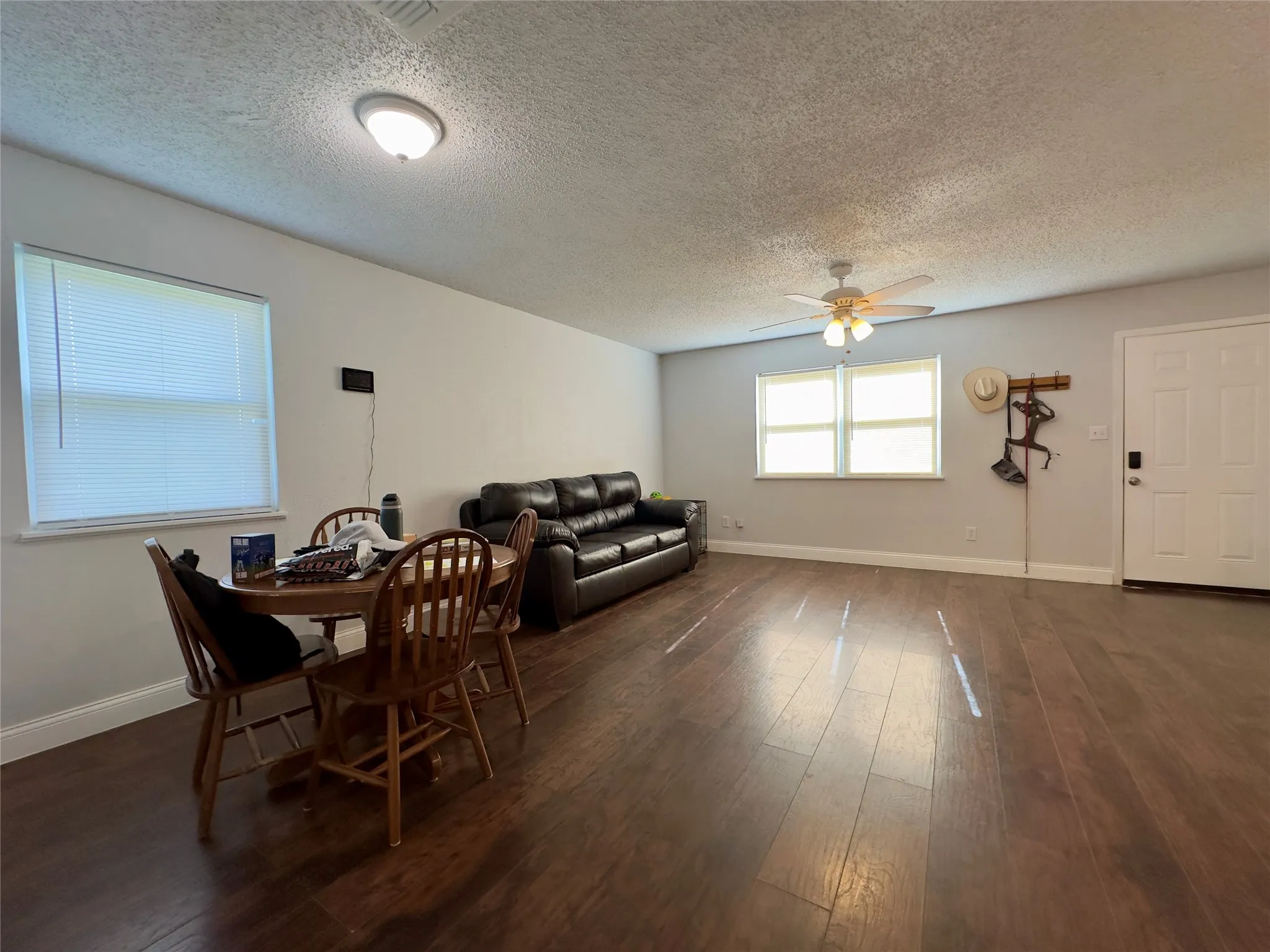 Spacious living area featuring wood-finish flooring, multiple windows, a ceiling fan, and a front entry door