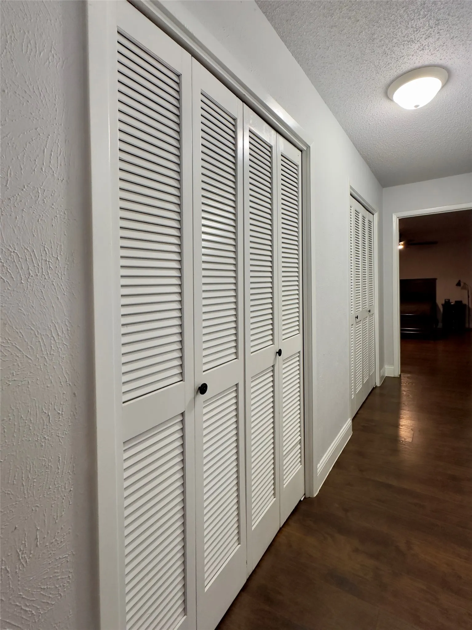 White louvered bifold doors, wood-finish flooring, and white wall trim