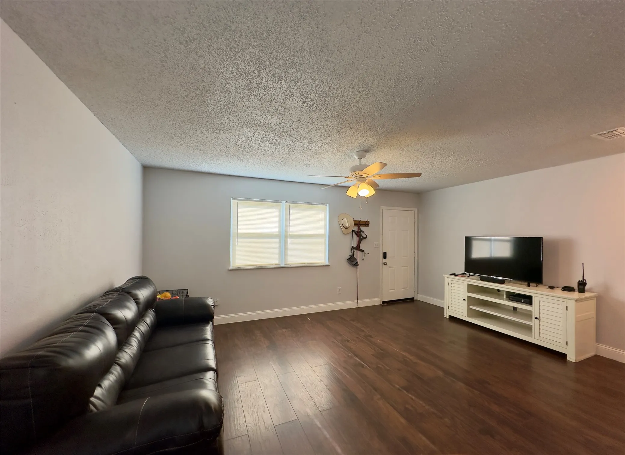Hardwood-finish flooring, two windows with blinds, ceiling fan with integrated lighting, and a paneled door