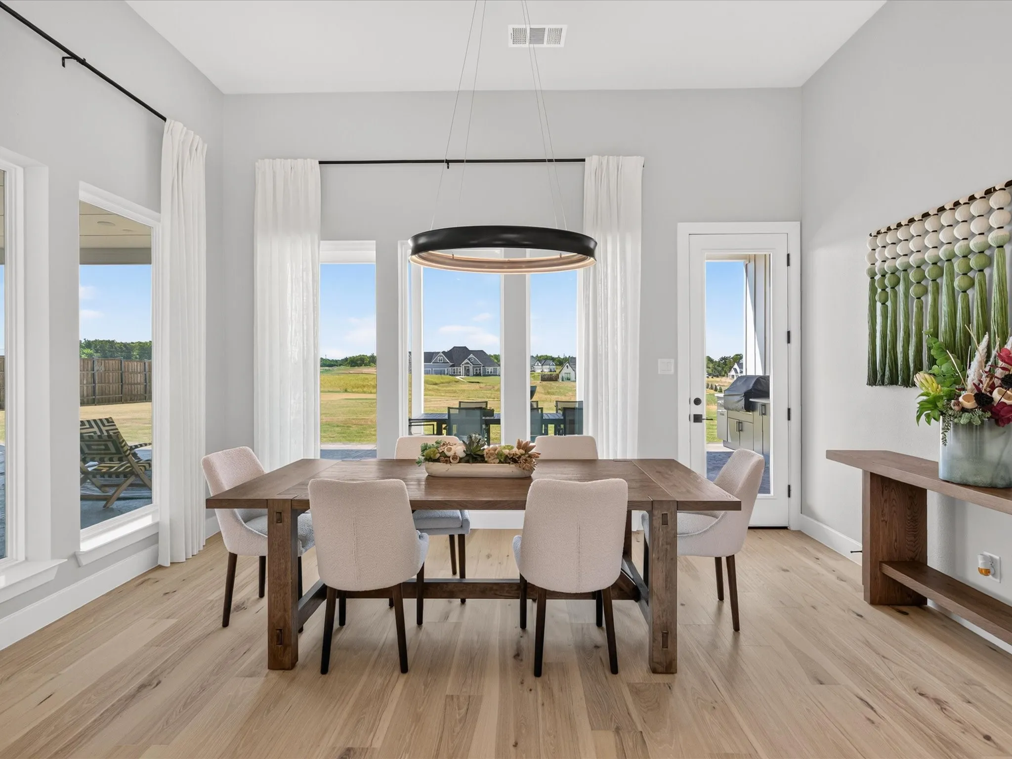 Spacious dining area featuring wood-finish flooring, a contemporary chandelier, multiple large windows, and a glass-paneled door