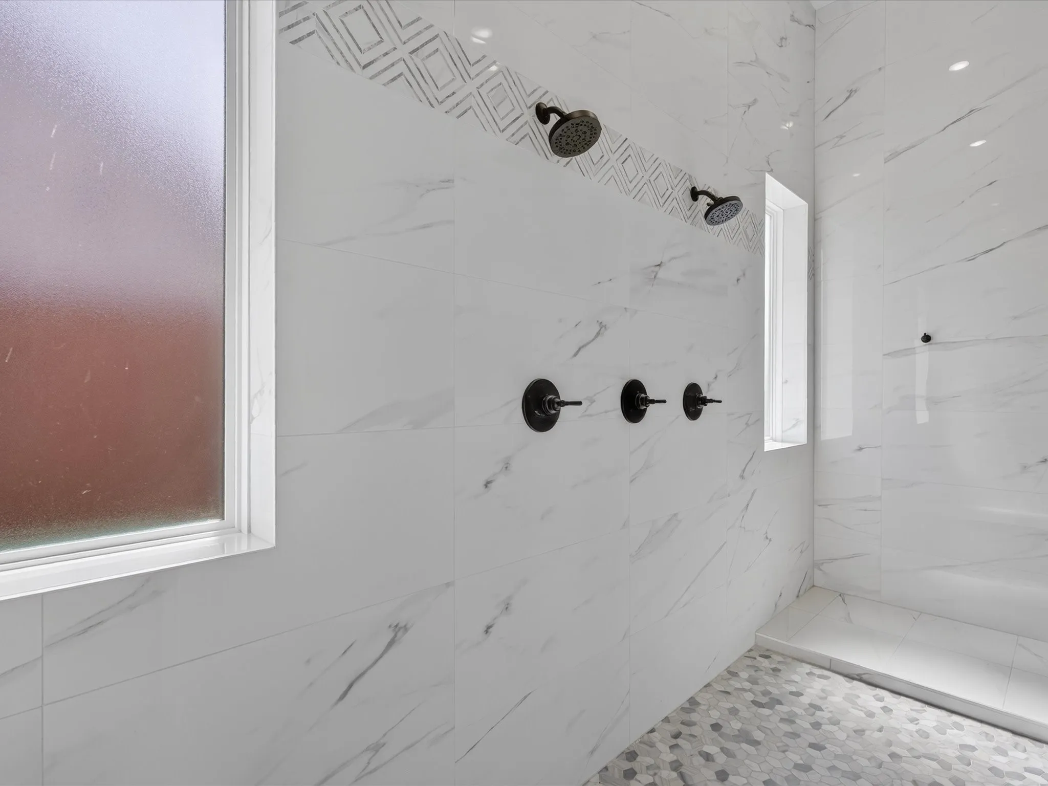 Shower with dual shower heads, matte black fixtures, marble-look tile walls, decorative accent tile band, and hexagonal mosaic floor