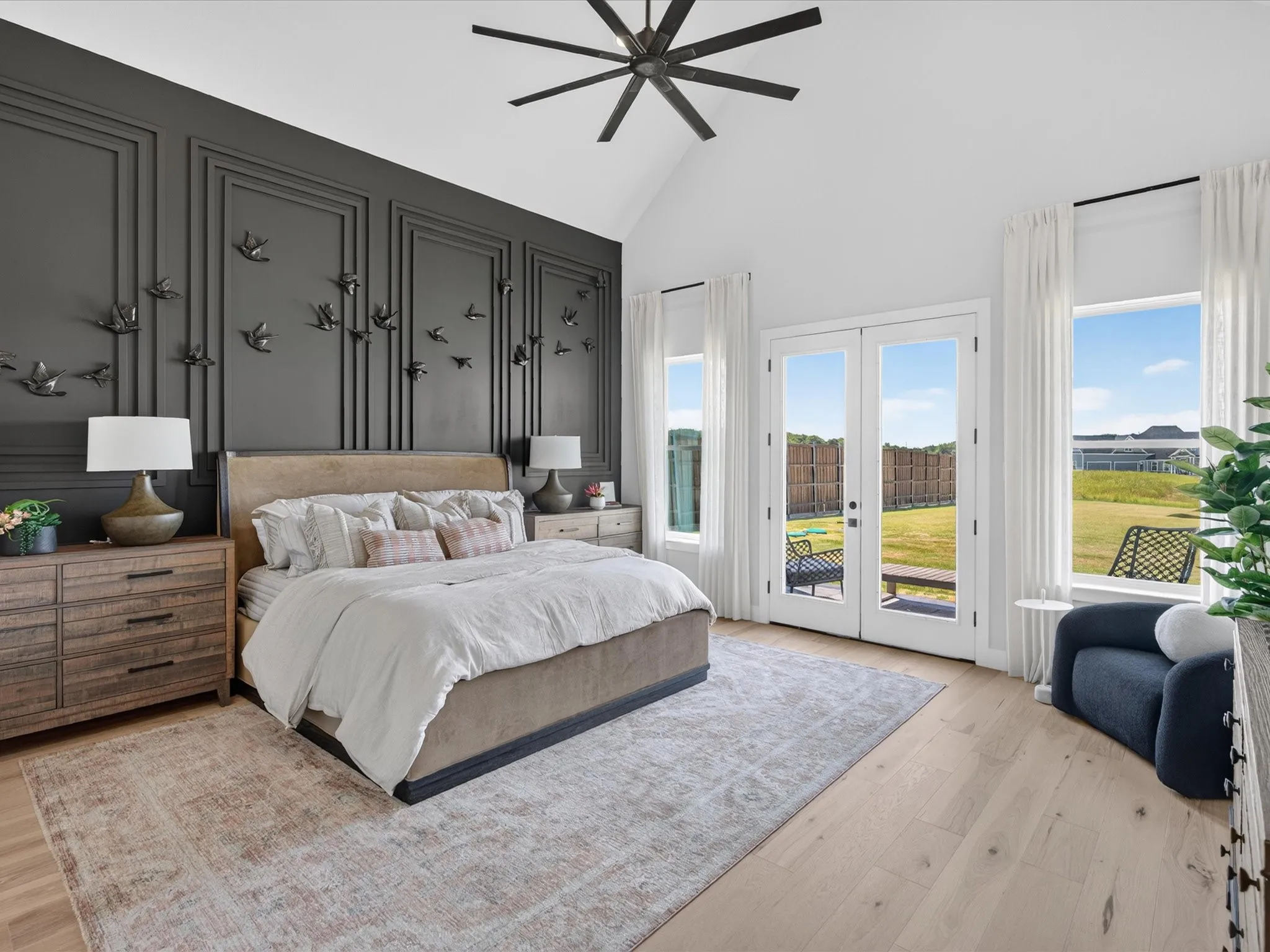 Vaulted ceiling with a contemporary ceiling fan, accent wall with decorative panel molding, light wood-finish flooring, and double French doors opening to the exterior