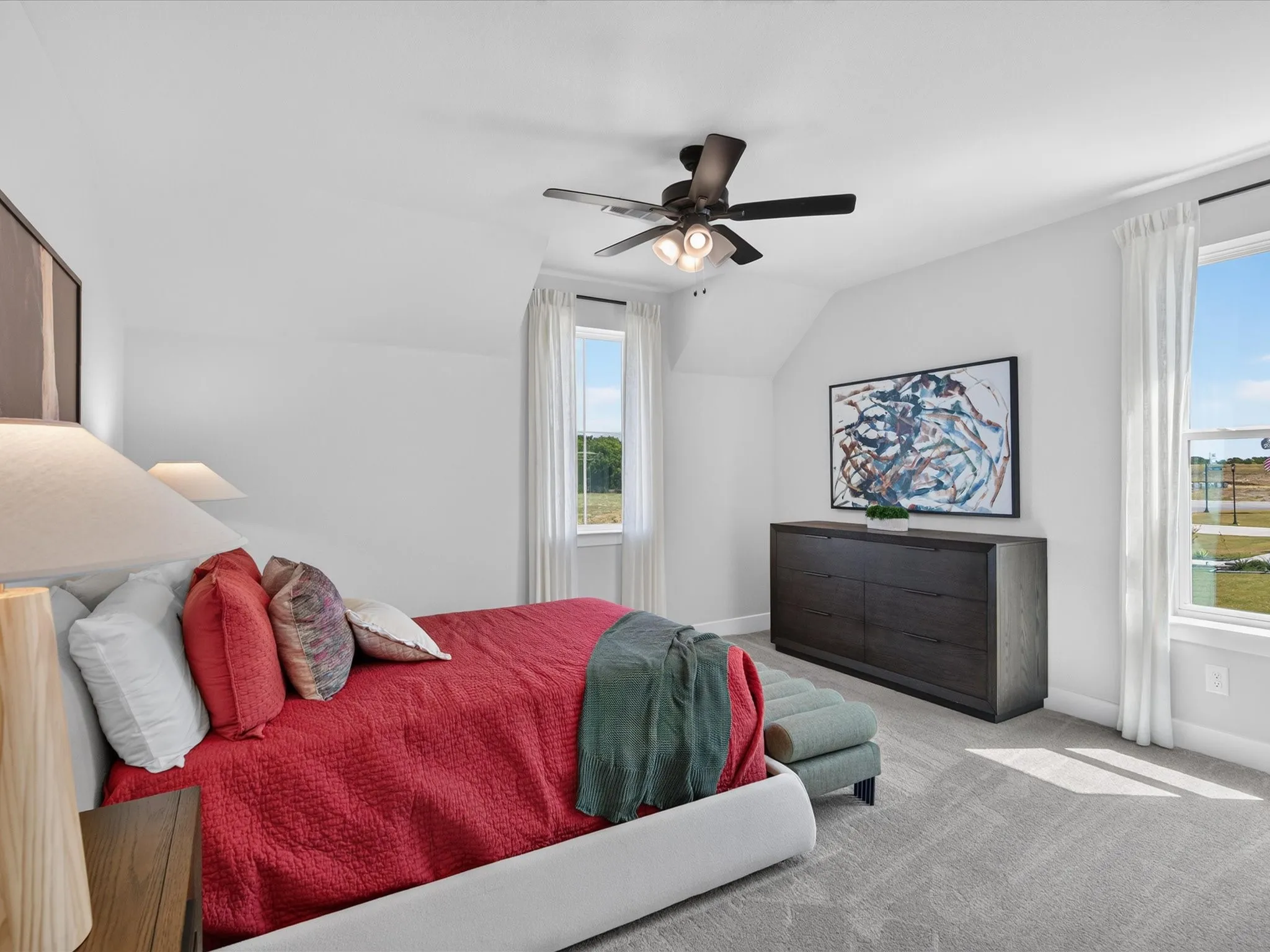 Carpeted room featuring a ceiling fan, two windows with white drapes, and sloped ceiling details