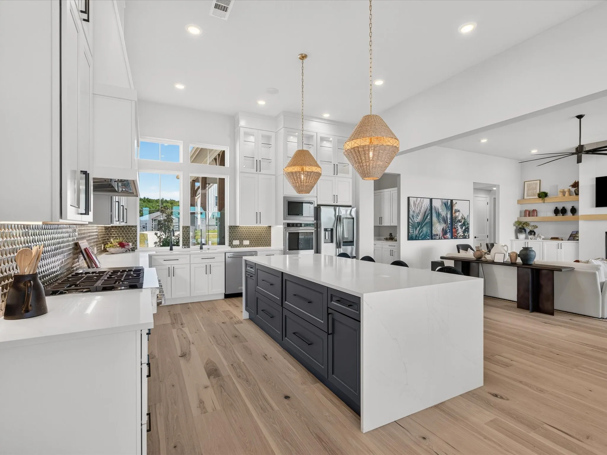 Spacious kitchen featuring an expansive center island, light wood-finish flooring, white cabinetry, integrated stainless steel appliances, and a gas range