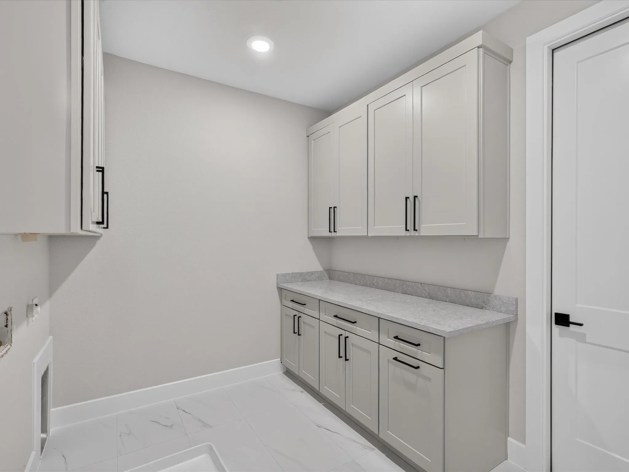 Light gray cabinetry with black hardware, complementing a light-toned countertop and white tile flooring