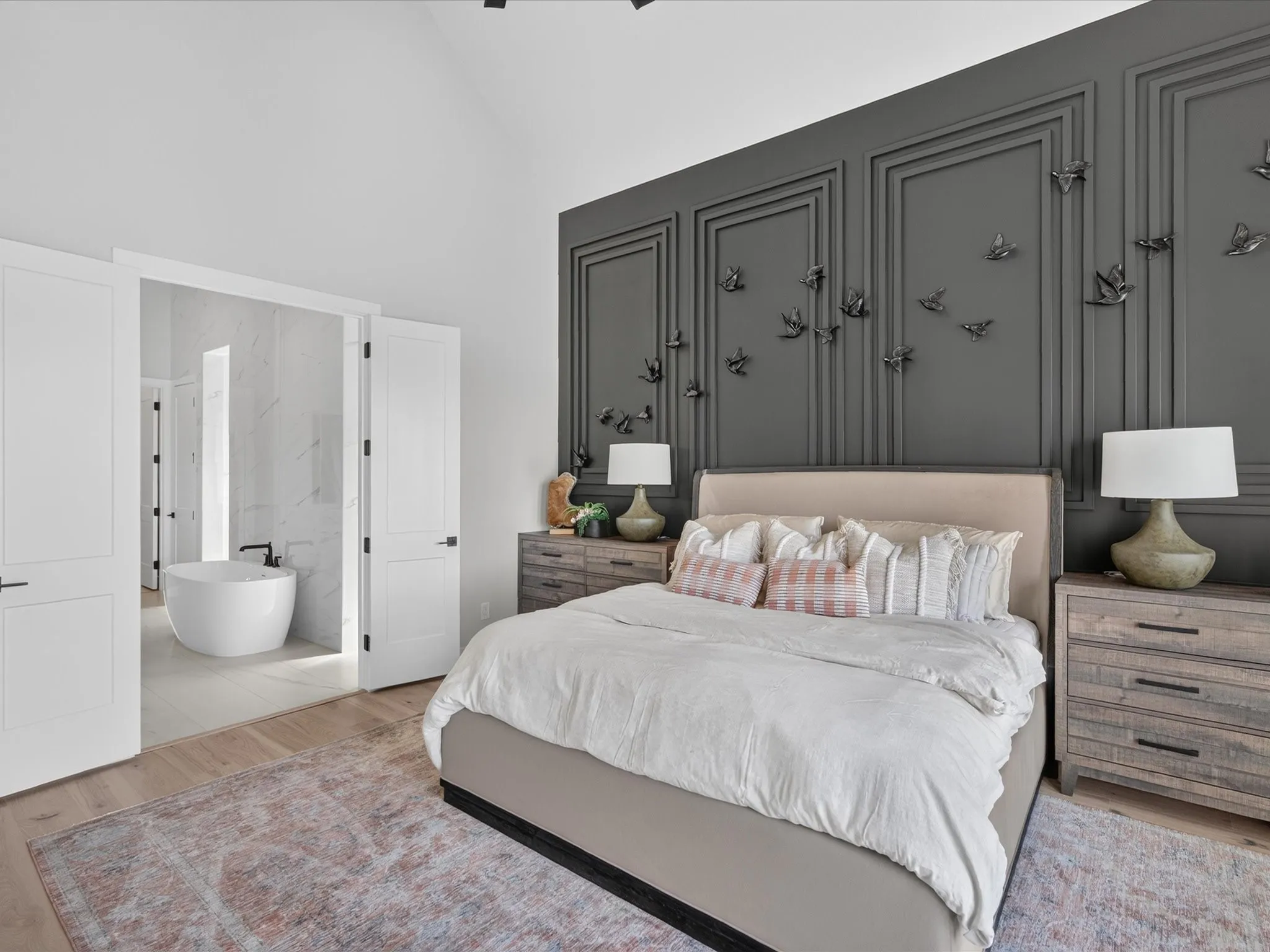 Vaulted ceiling, wood-finish flooring, accent wall with decorative molding, freestanding soaking tub, and double entry doors