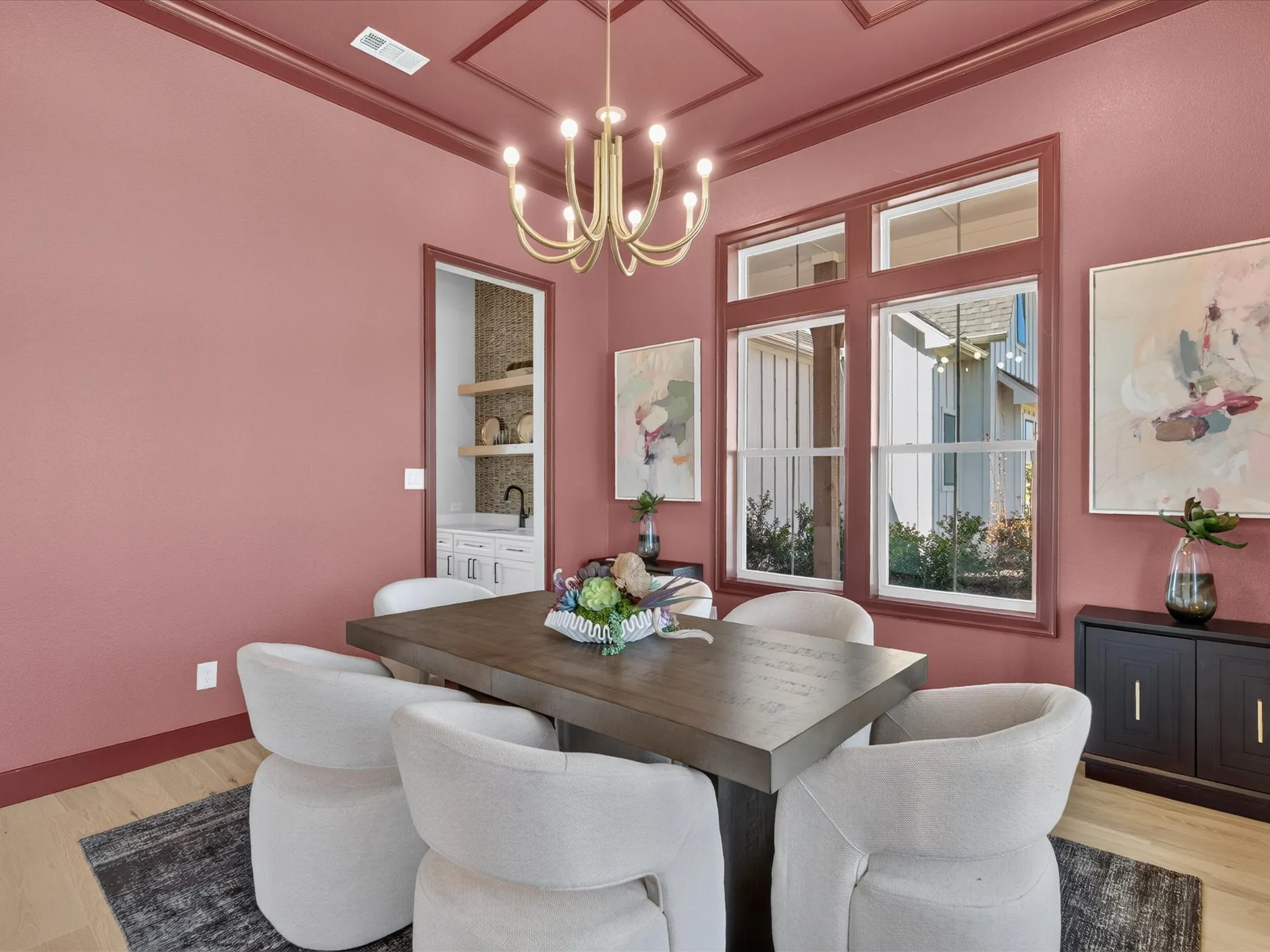 Tray ceiling with decorative molding, wood-finish flooring, gold-tone chandelier, and a built-in wet bar with open shelving