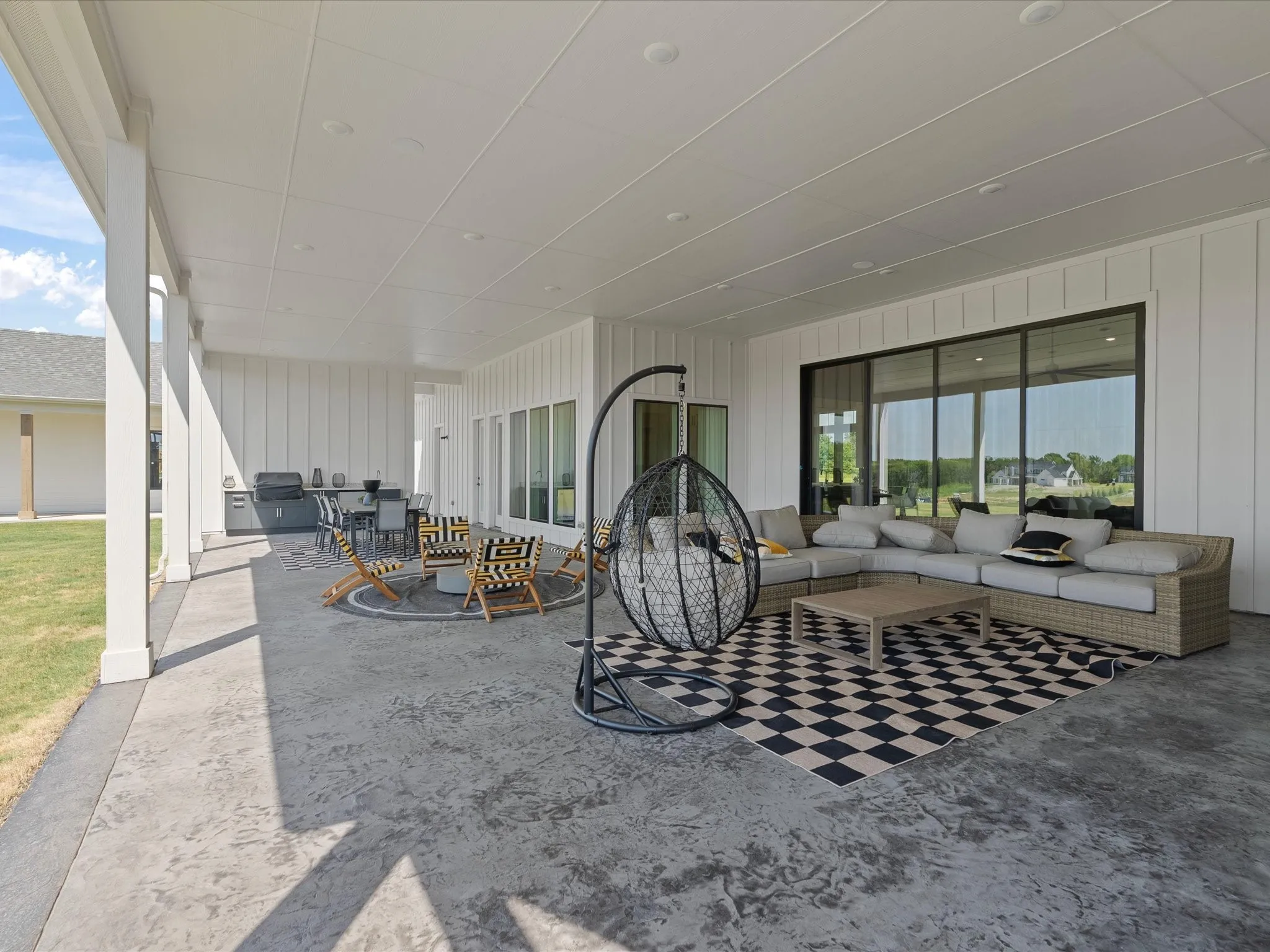 Expansive covered patio featuring a stamped concrete surface, recessed lighting, white board and batten siding, and large sliding glass doors
