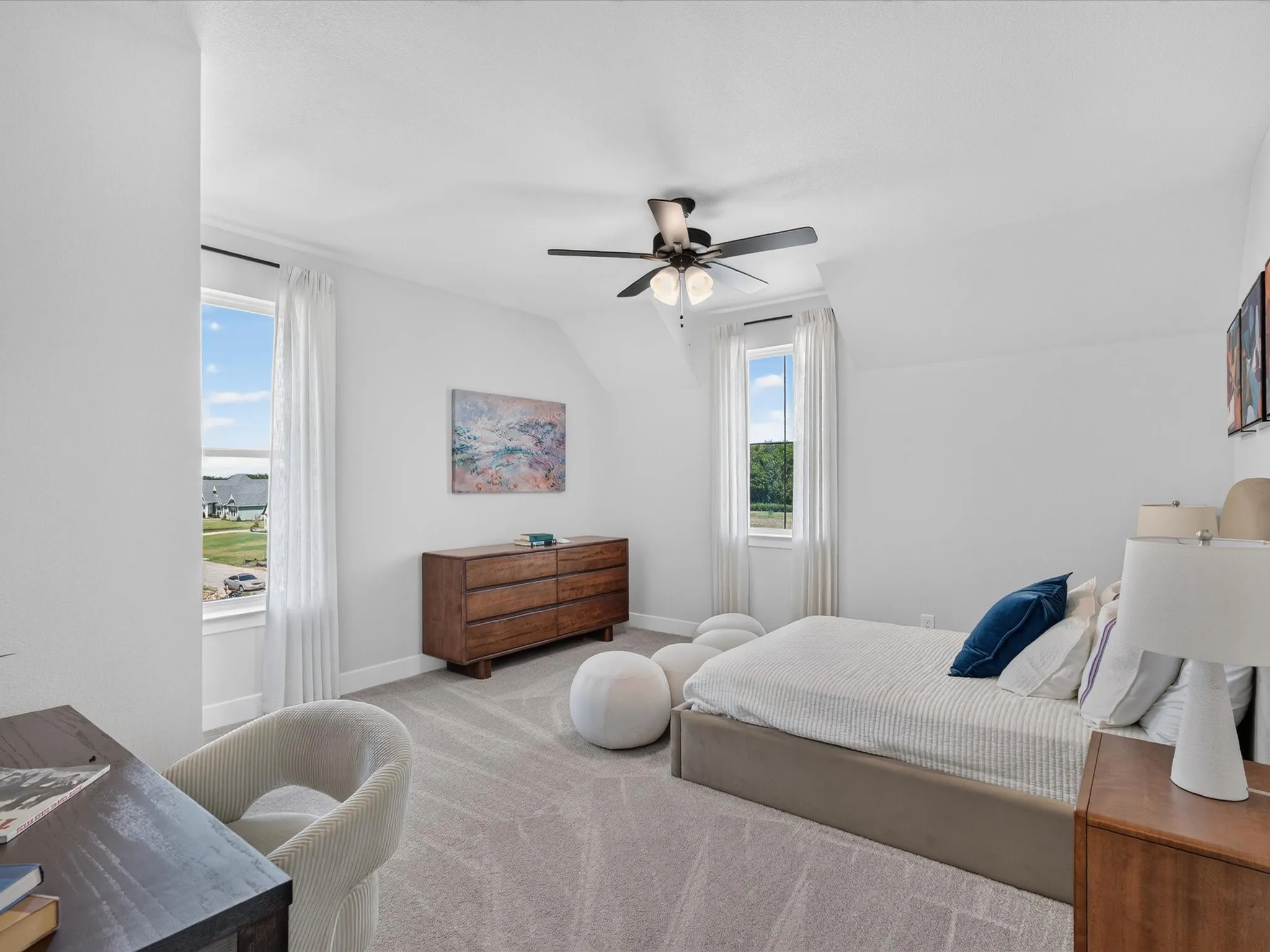 Spacious room with sloped ceilings, two large windows, a ceiling fan with integrated lighting, and neutral carpeting