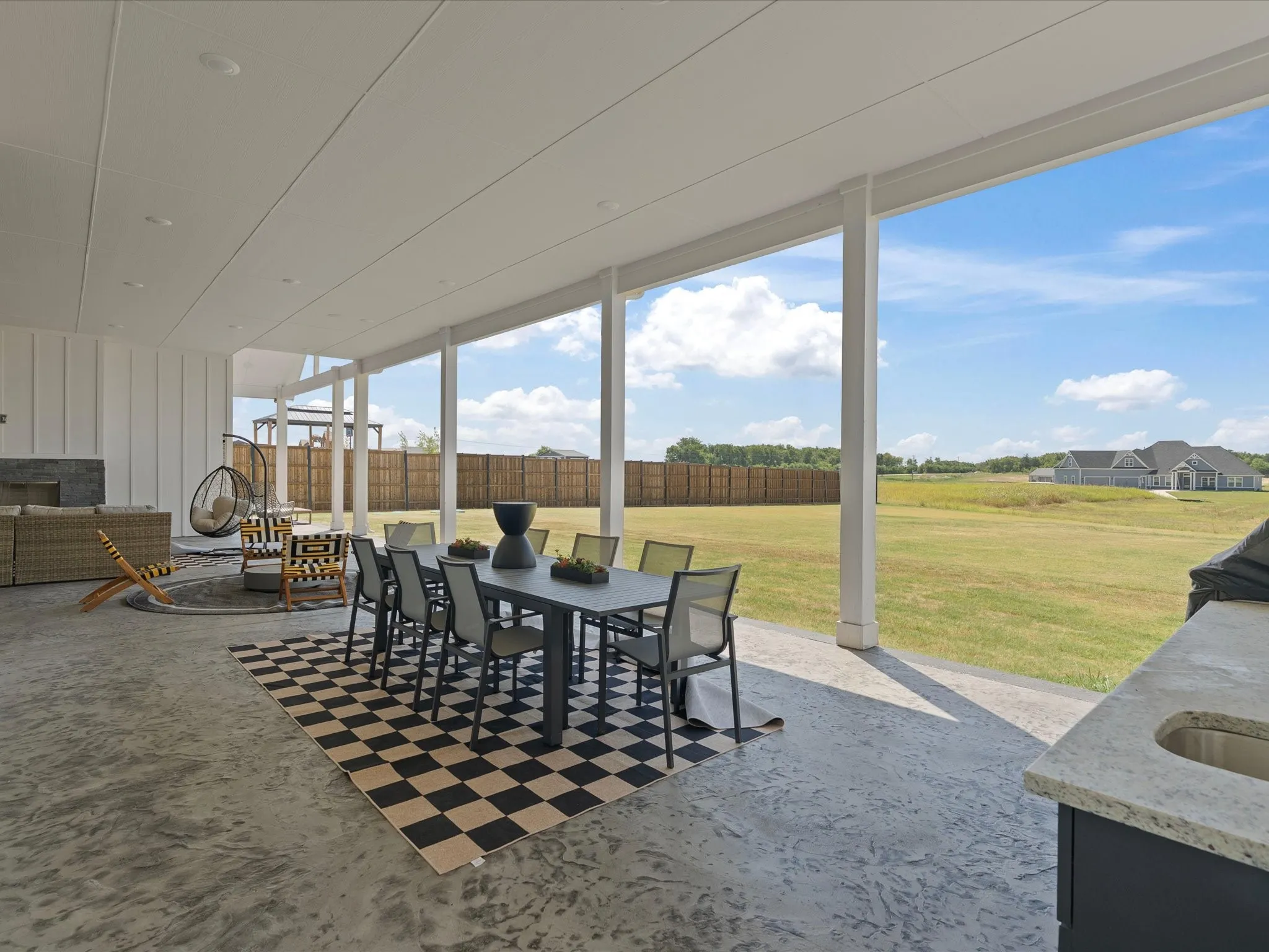 Expansive covered patio with a stamped concrete surface, a built-in outdoor kitchen with a sink, and a dedicated outdoor fireplace feature