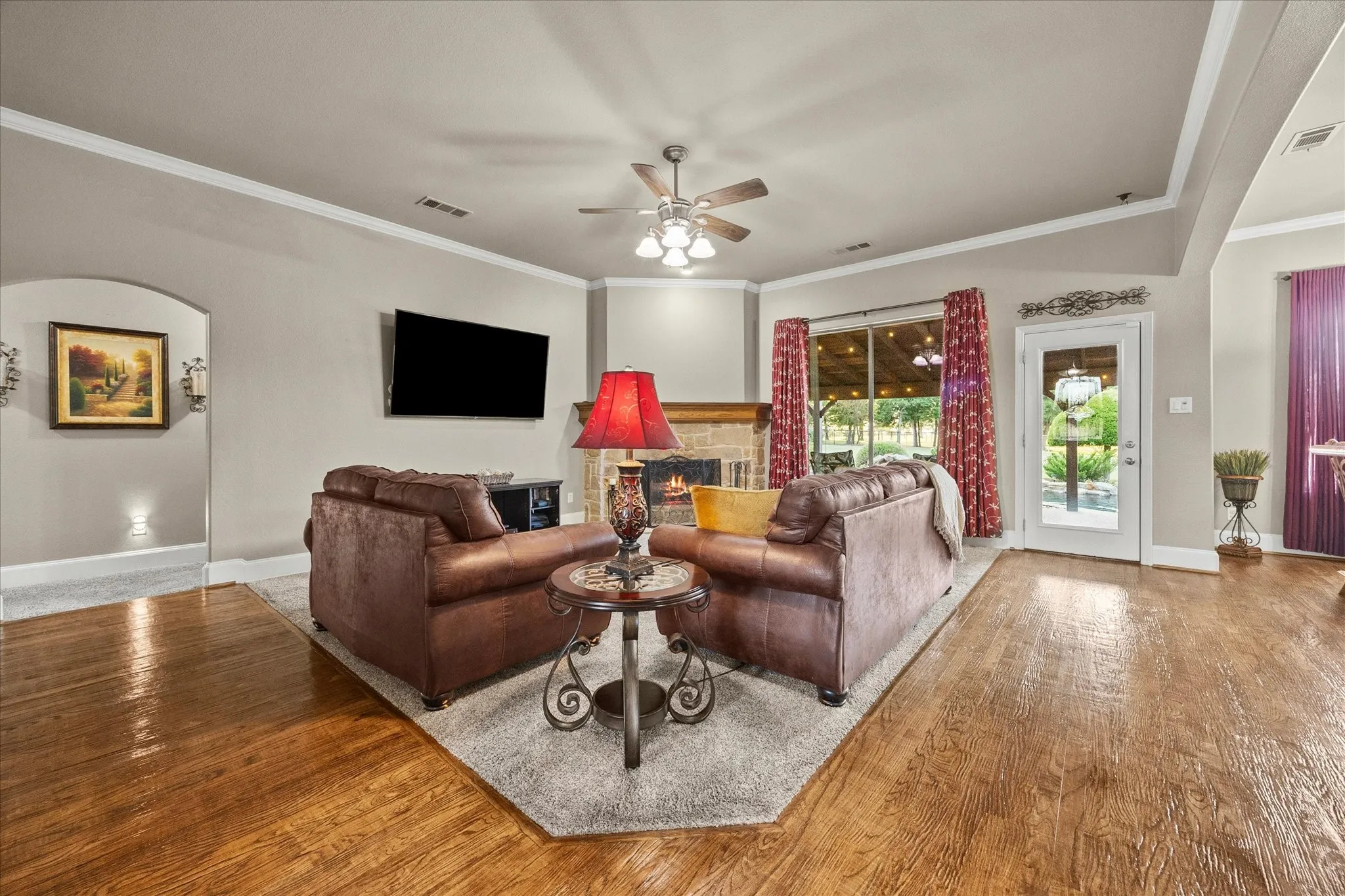 Hardwood flooring, fireplace with stone surround, crown molding, ceiling fan, and French door with glass panels