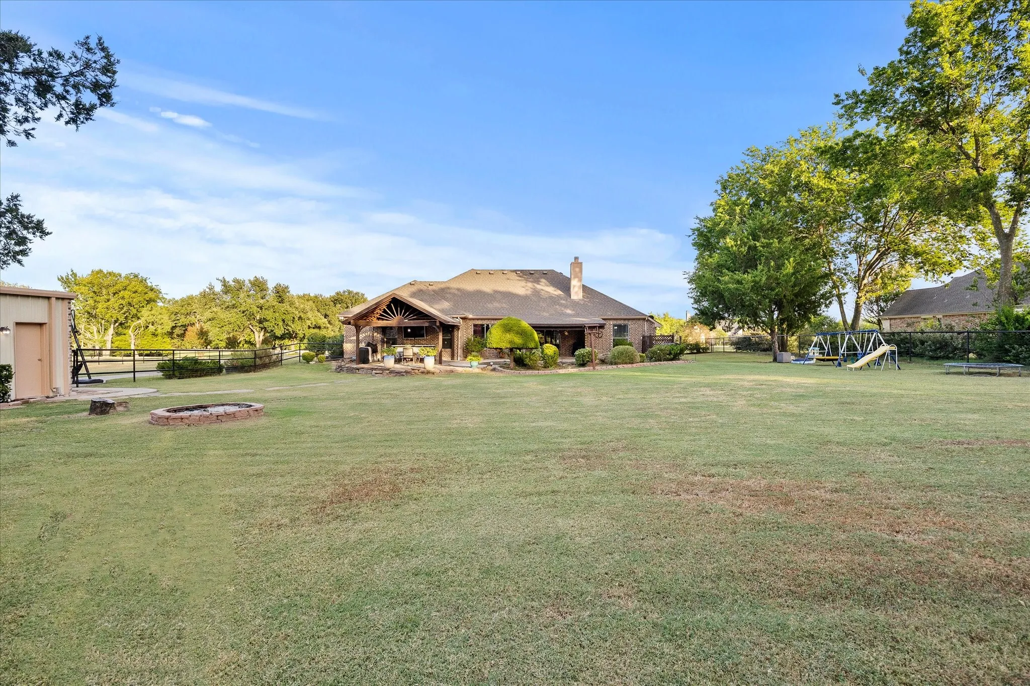 Expansive green lawn with mature trees, a detached storage building, and a fire pit