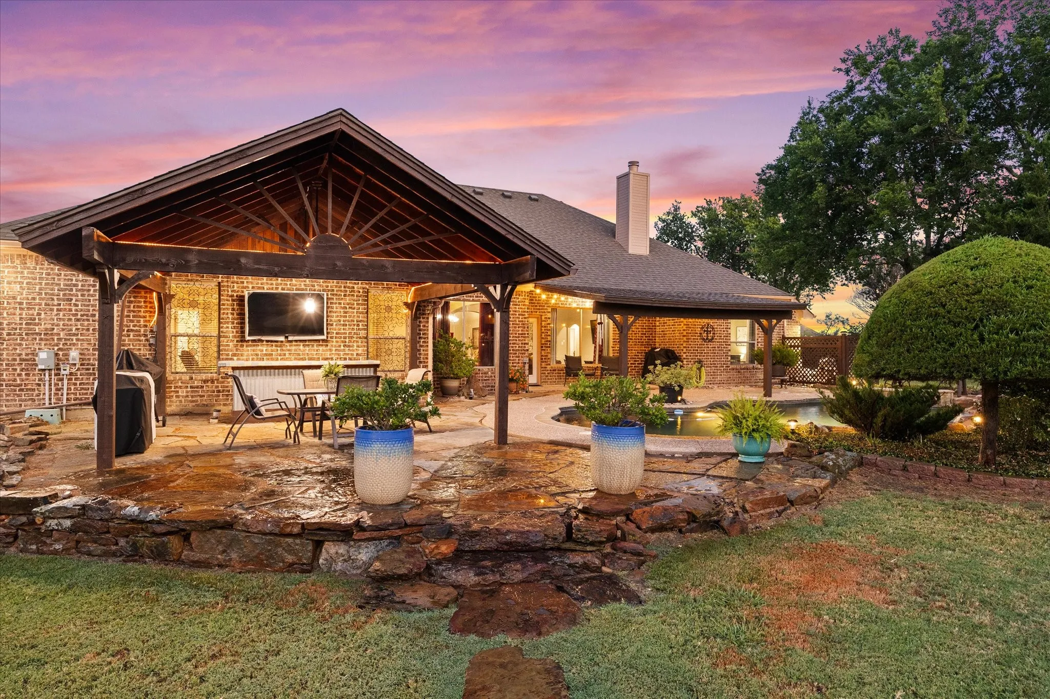 Expansive patio featuring a wood-beam covered structure, stone paver flooring, brick exterior, and a stone retaining wall