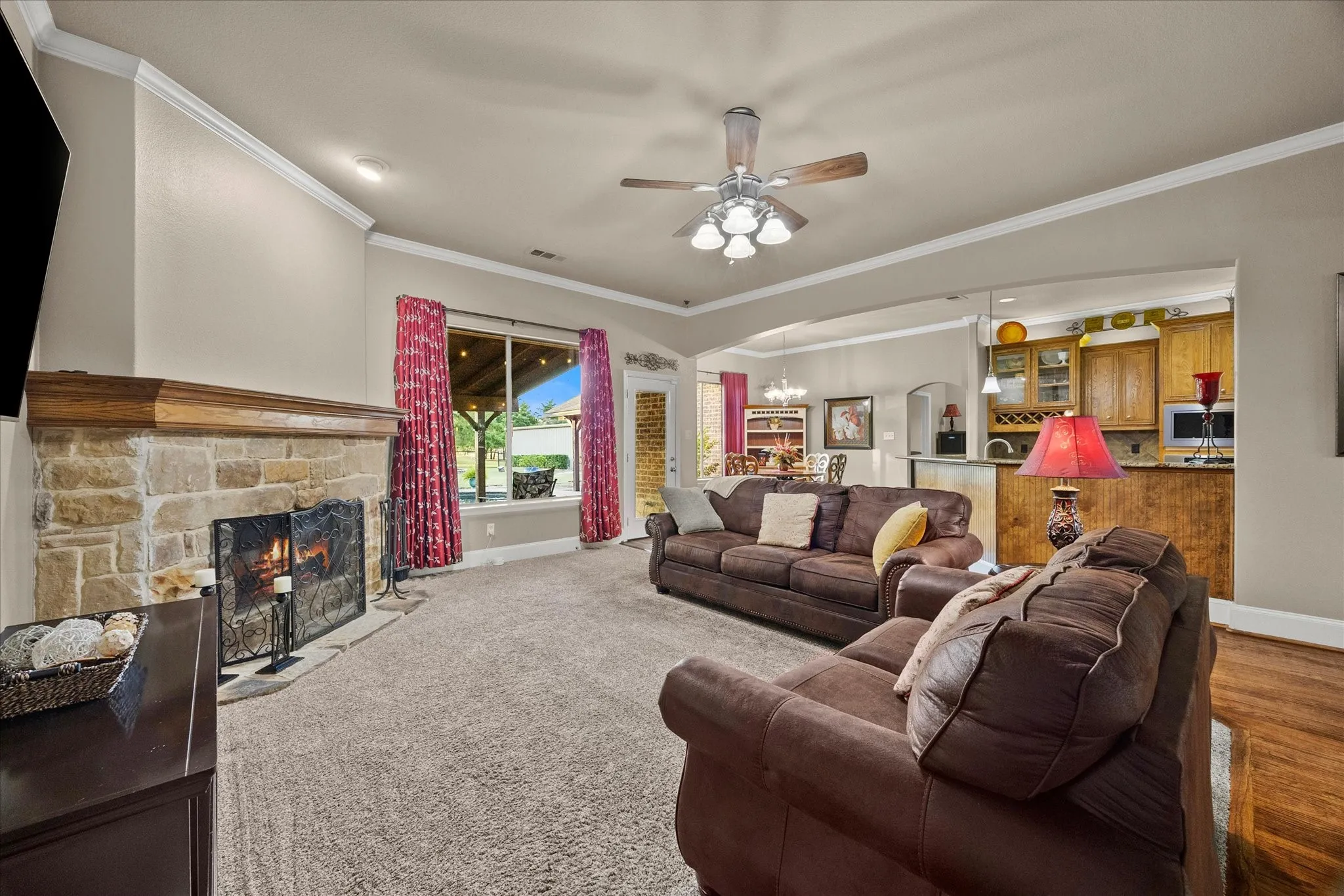 Stone-clad fireplace with a wood mantle, ceiling fan, and large window with outdoor access