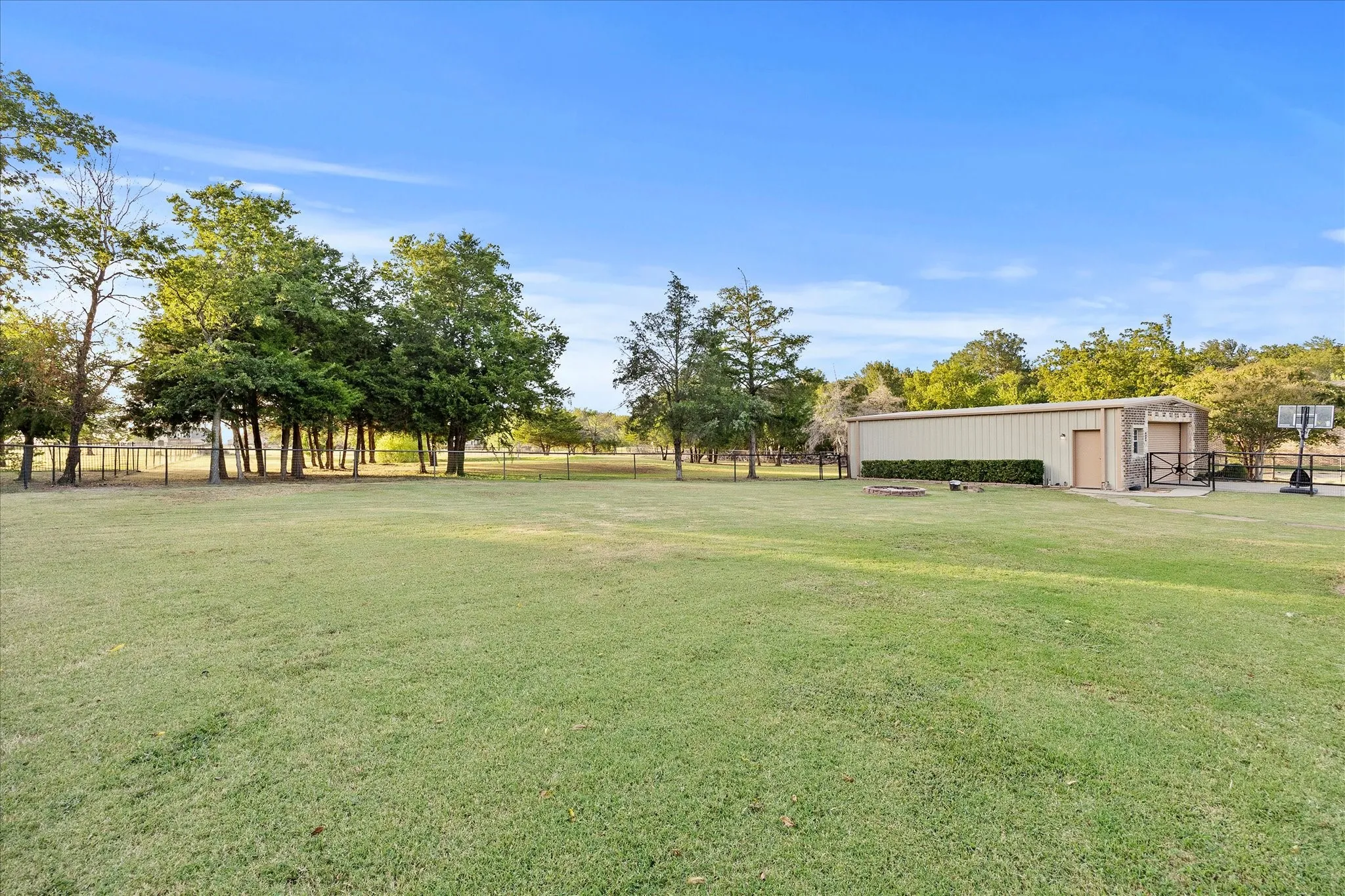 Expansive grassy lawn with mature trees and a large metal outbuilding