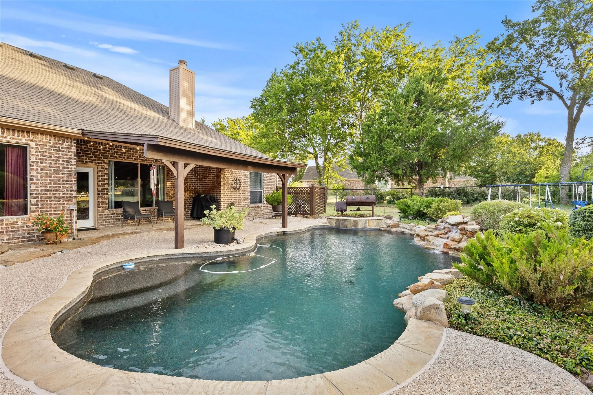 Brick exterior with a covered patio, freeform swimming pool, and rock waterfall feature