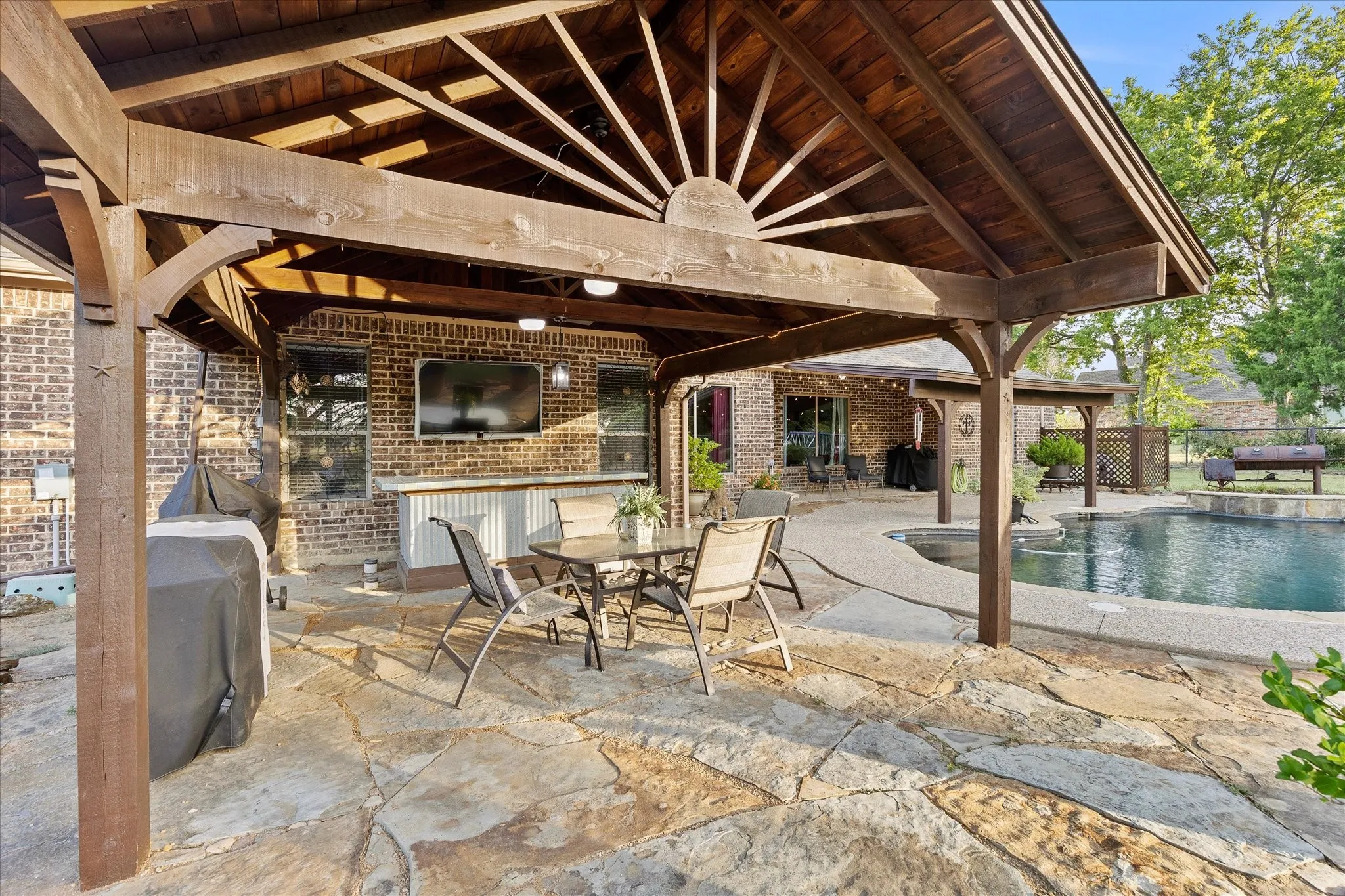 Expansive flagstone patio with a substantial wooden pergola, a built-in outdoor bar with a stone countertop, and a shaped swimming pool