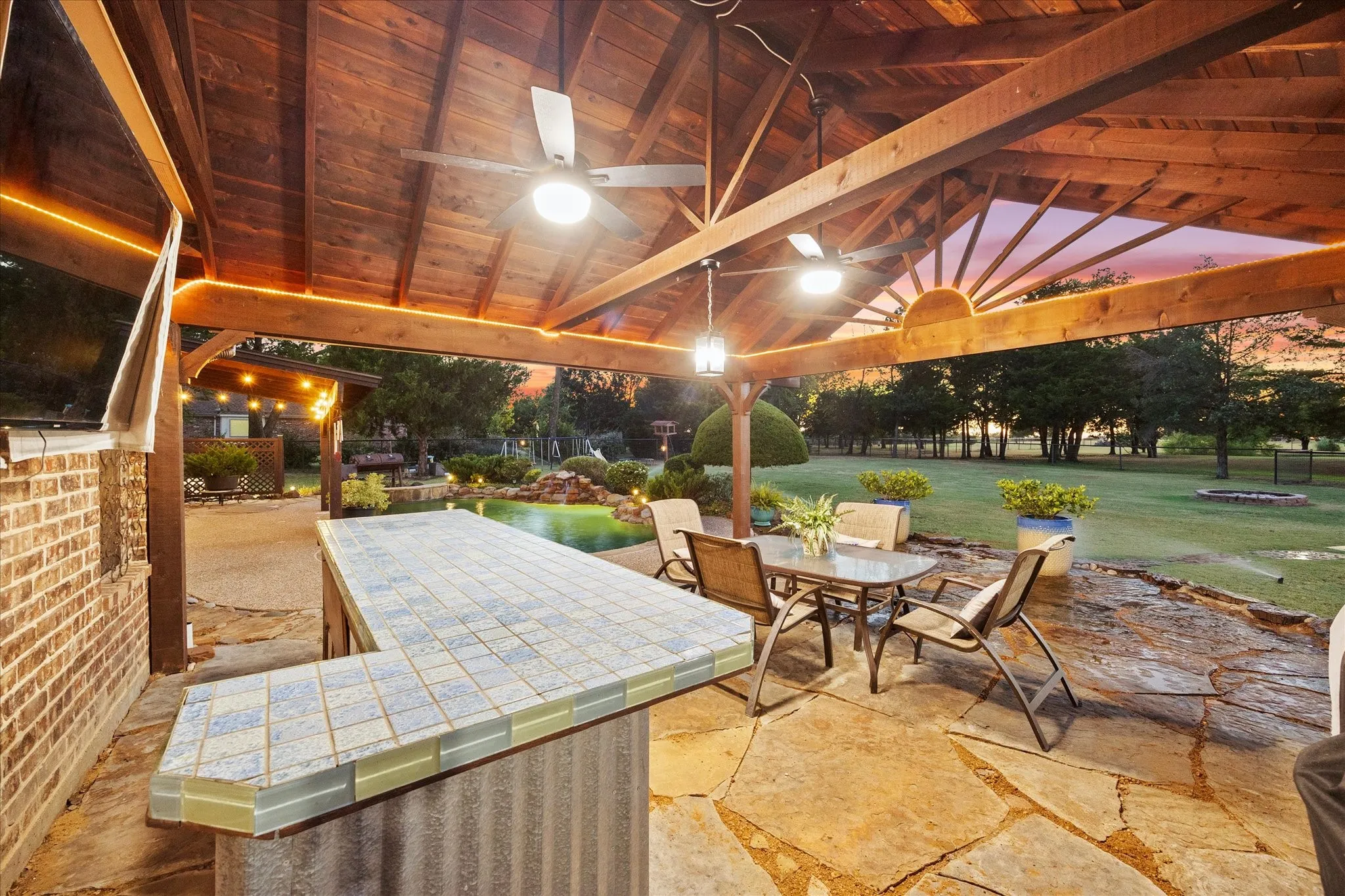 Covered patio featuring a wood-beamed ceiling, ceiling fans, and an integrated outdoor bar with tiled countertop