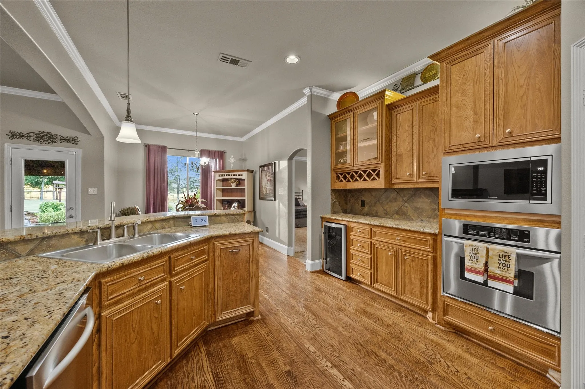Kitchen featuring wood-finish flooring, light-toned cabinetry, granite countertops, and stainless steel appliances including a built-in oven and microwave
