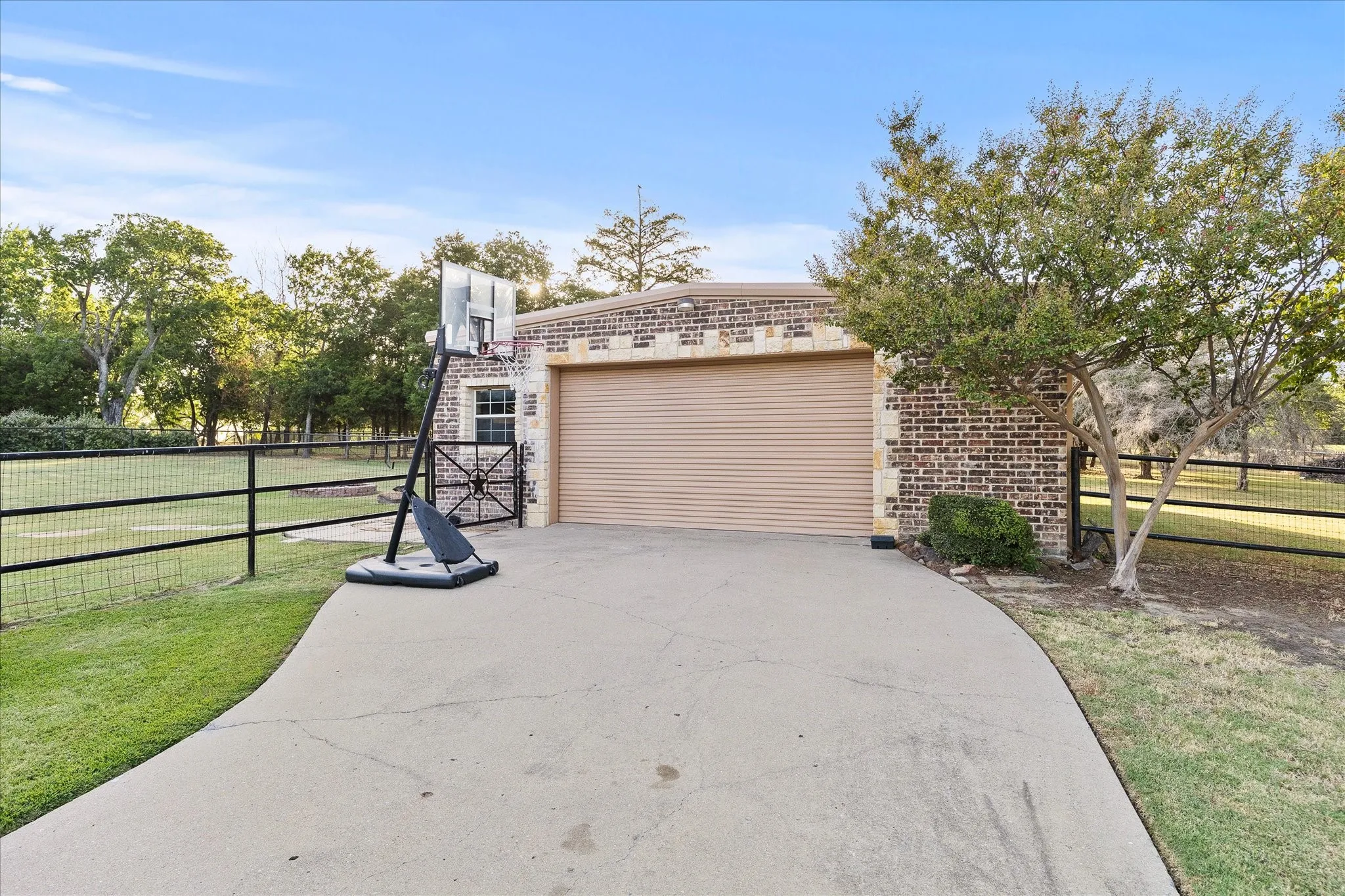 Brick and stone exterior building with a roll-up garage door, concrete driveway, and black metal fencing