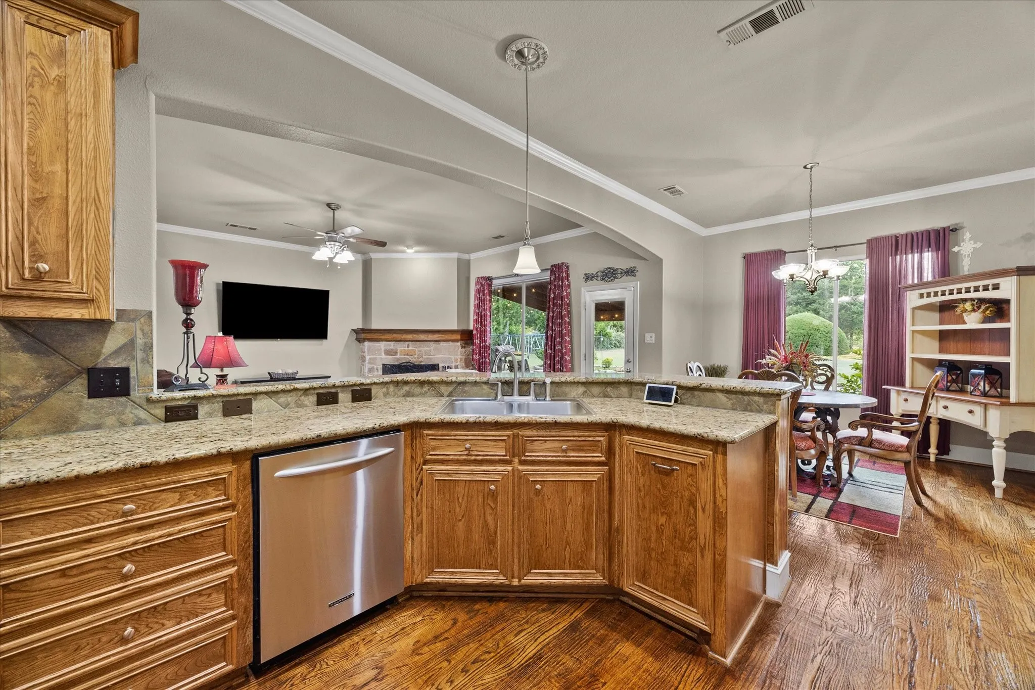 Kitchen featuring wood cabinetry, stainless steel dishwasher, an undermount sink, and stone countertops with a complementary tile backsplash