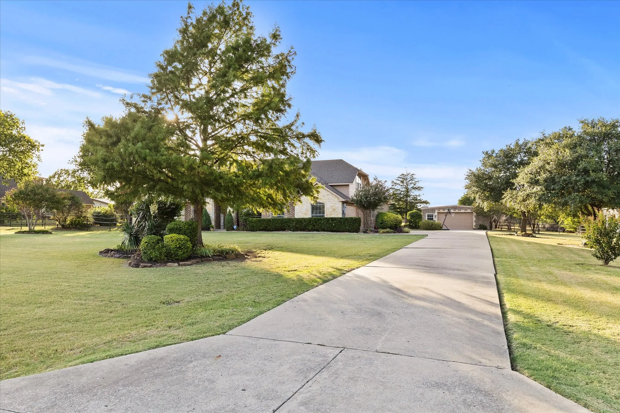 Manicured front yard with mature trees, established landscaping, and a long concrete driveway