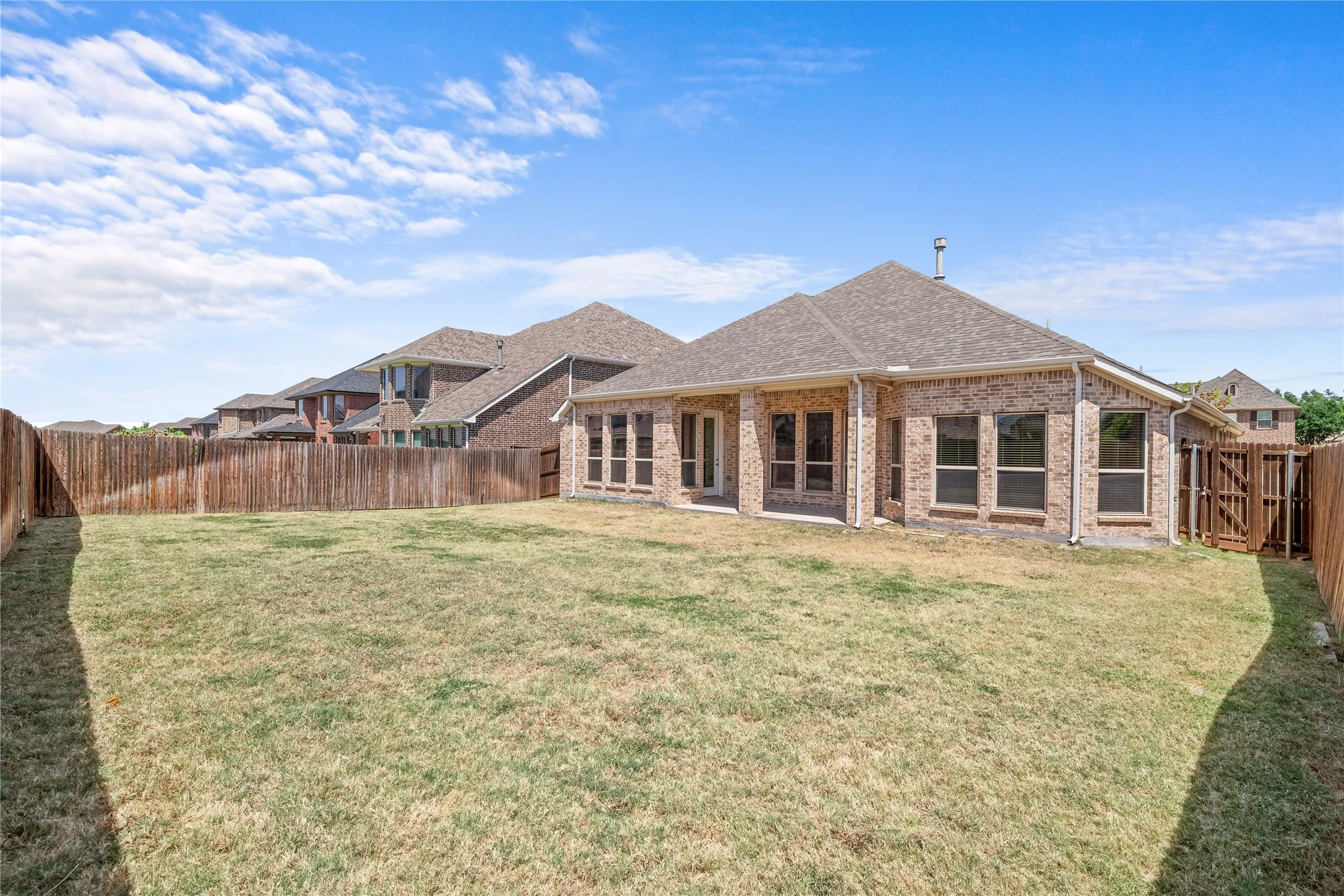 Expansive backyard with a full privacy fence, brick exterior, and multiple windows