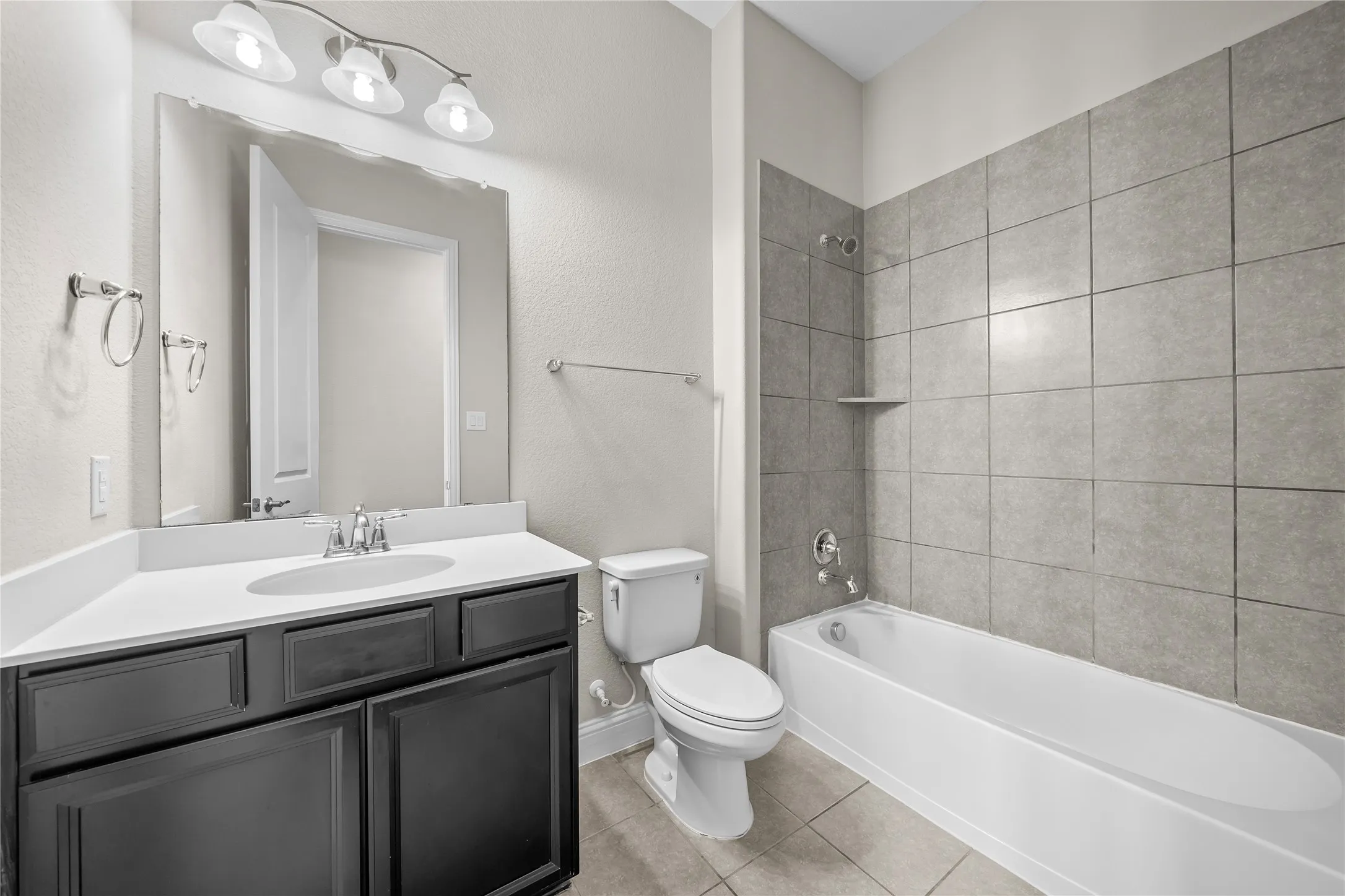 Modern bathroom featuring a dark wood vanity with dual sink configuration, large framed mirror with integrated lighting, ceramic tile flooring, subway tile shower surround with glass enclosure, and white soaking tub with chrome fixtures