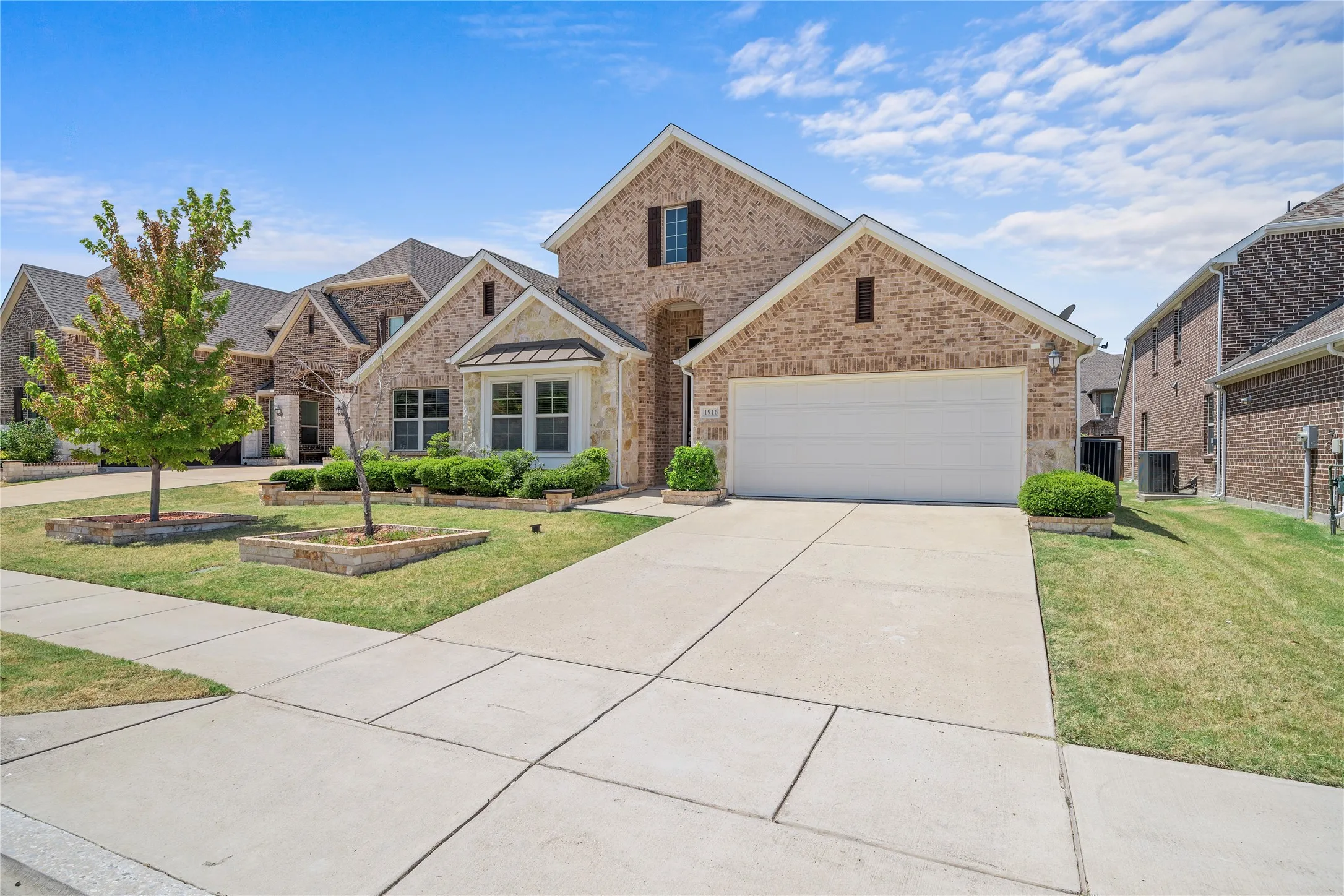 Brick and stone exterior featuring a two-car garage, concrete driveway, and front landscaping
