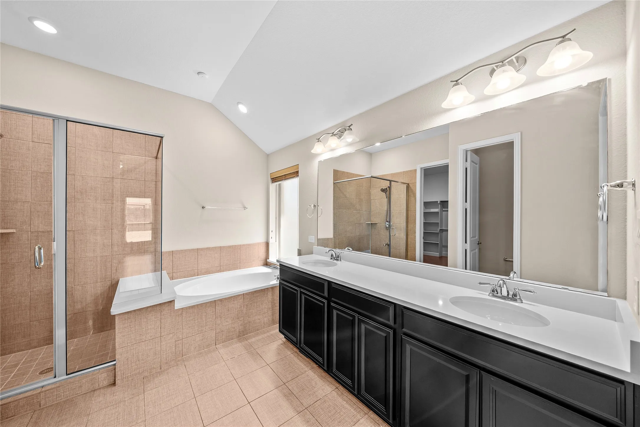 Dual vanity with undermount sinks, spacious mirror, tiled shower enclosure with glass door, built-in soaking tub, and tile flooring