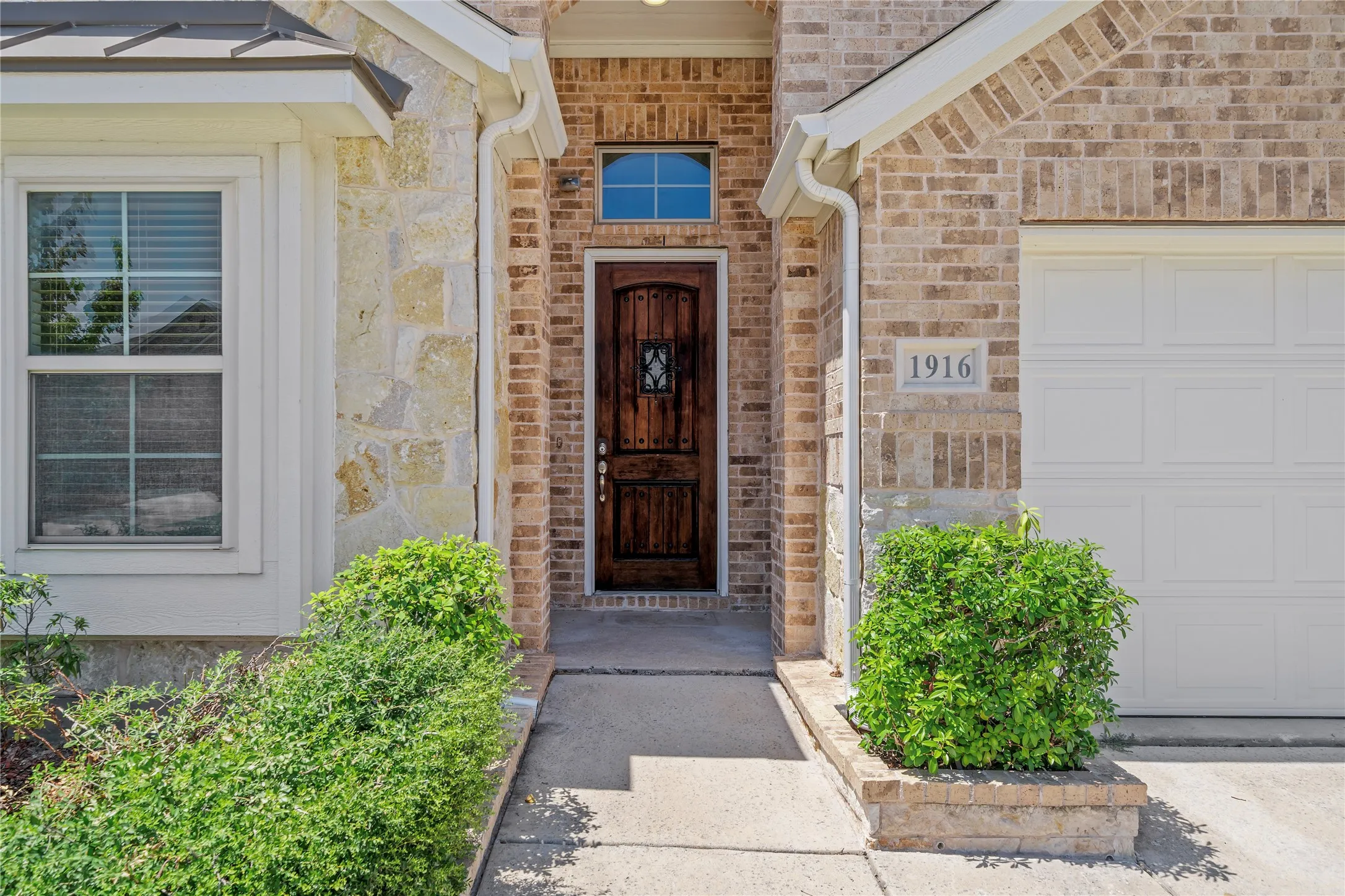 Brick and stone exterior with a wood-panel entry door, transom window, and an attached garage
